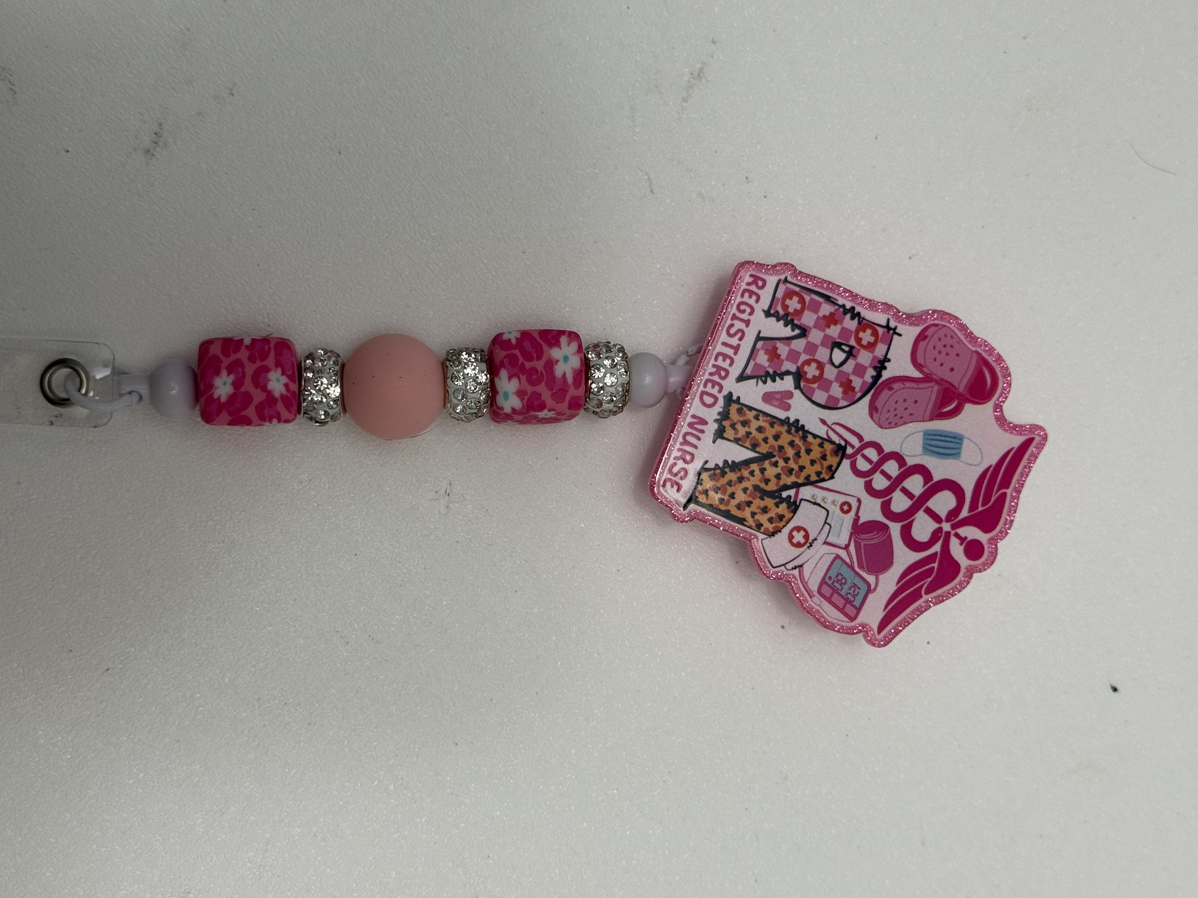 Pink beaded badge reel with floral cube beads, silver glitter spacers, and a Registered Nurse charm