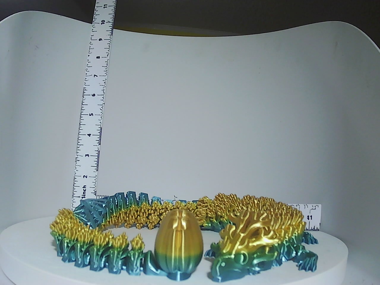 Teal and gold articulated dragon coiled around a golden egg on a white display stand