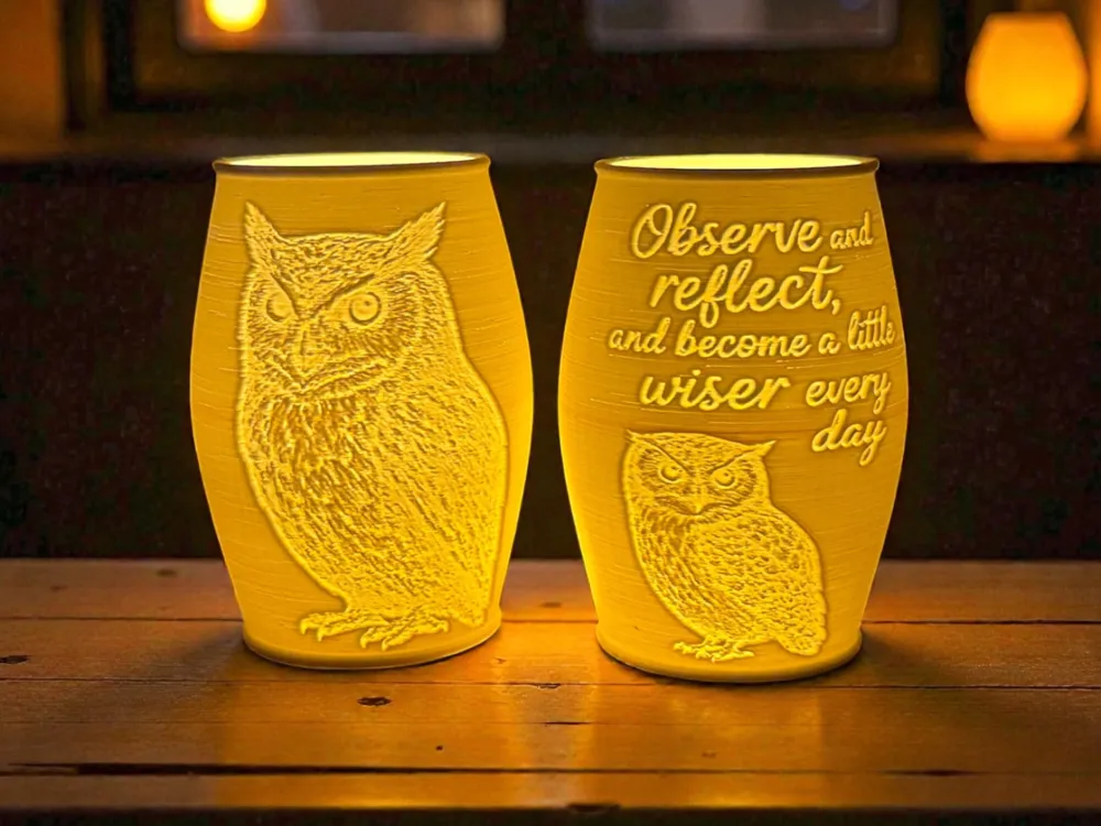 Two glowing owl candle lanterns on a wood table showing owl portrait and wisdom quote sides