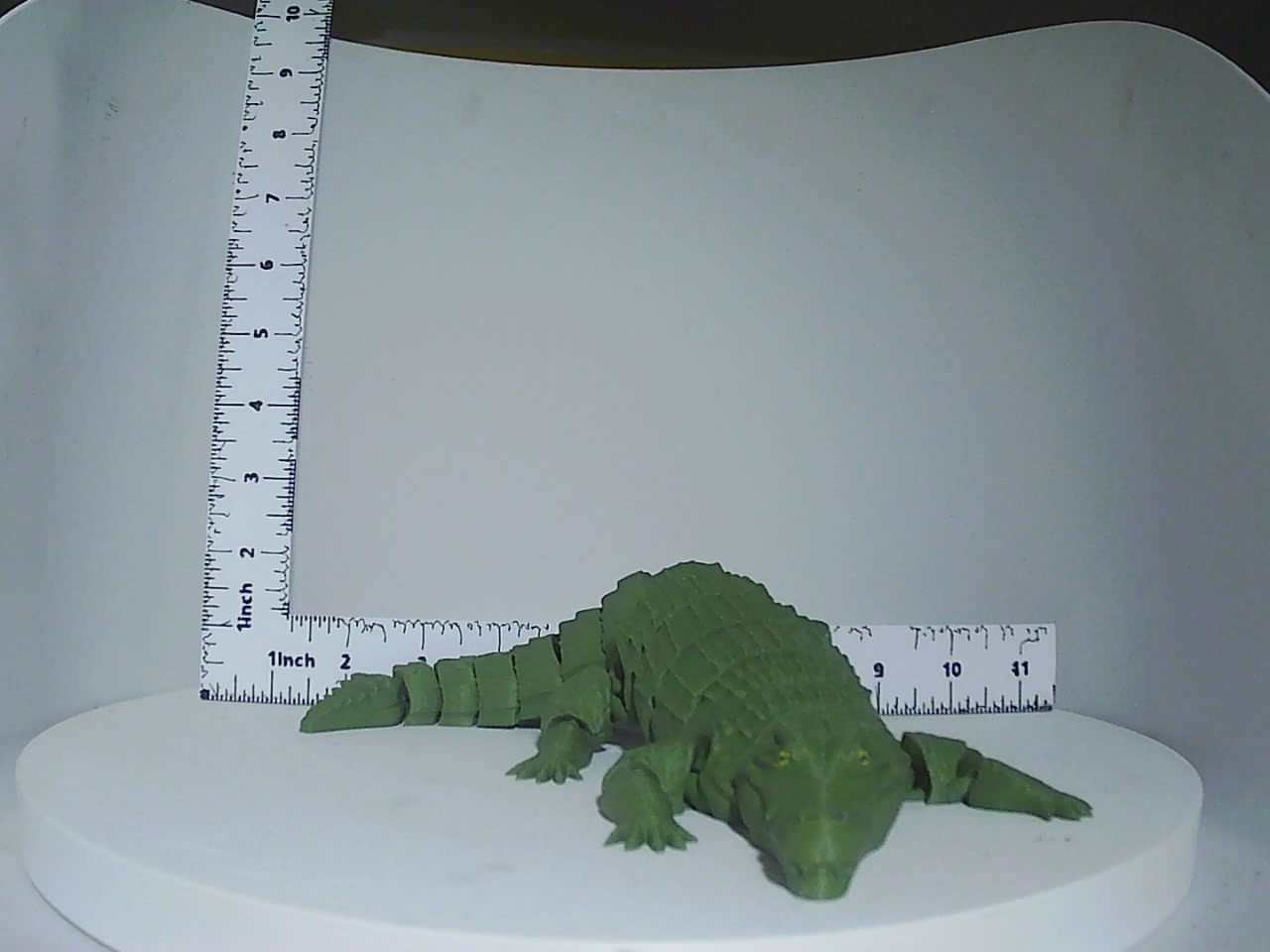 Forest green articulated 3D printed crocodile figure shown next to a ruler for scale