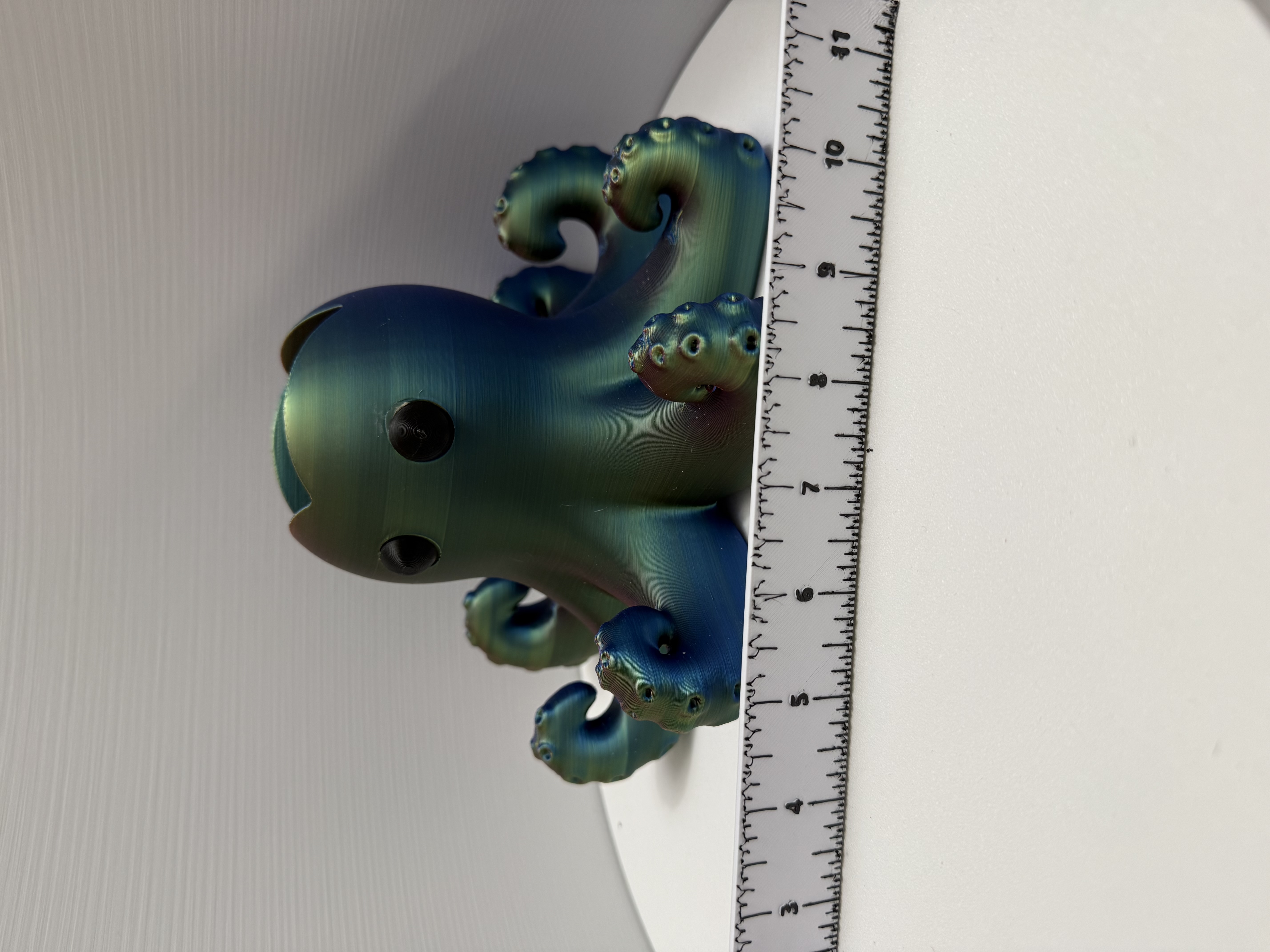 Side view of iridescent teal-green octopus figurine with ruler showing width