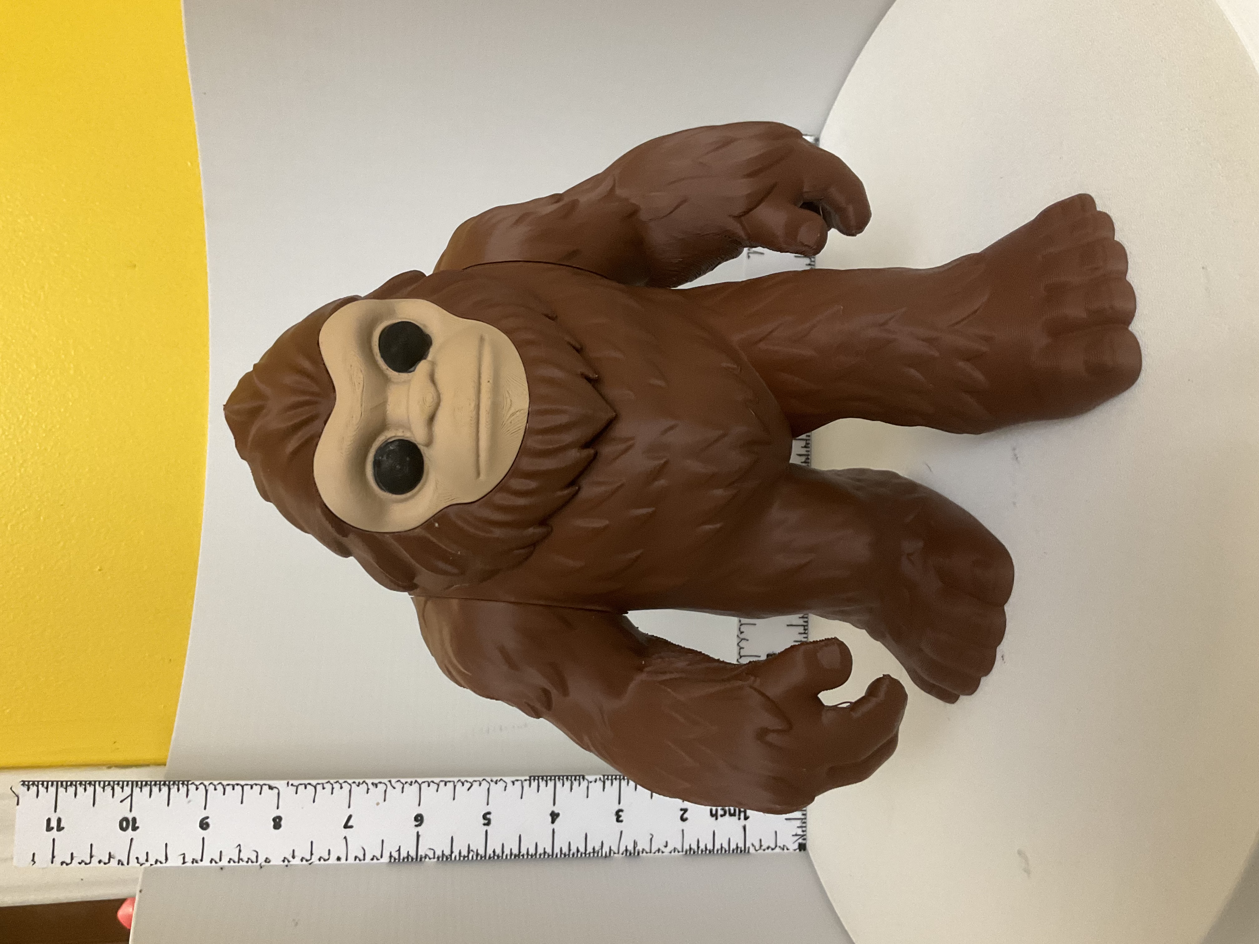 Brown bigfoot sasquatch figure standing upright beside a ruler for scale