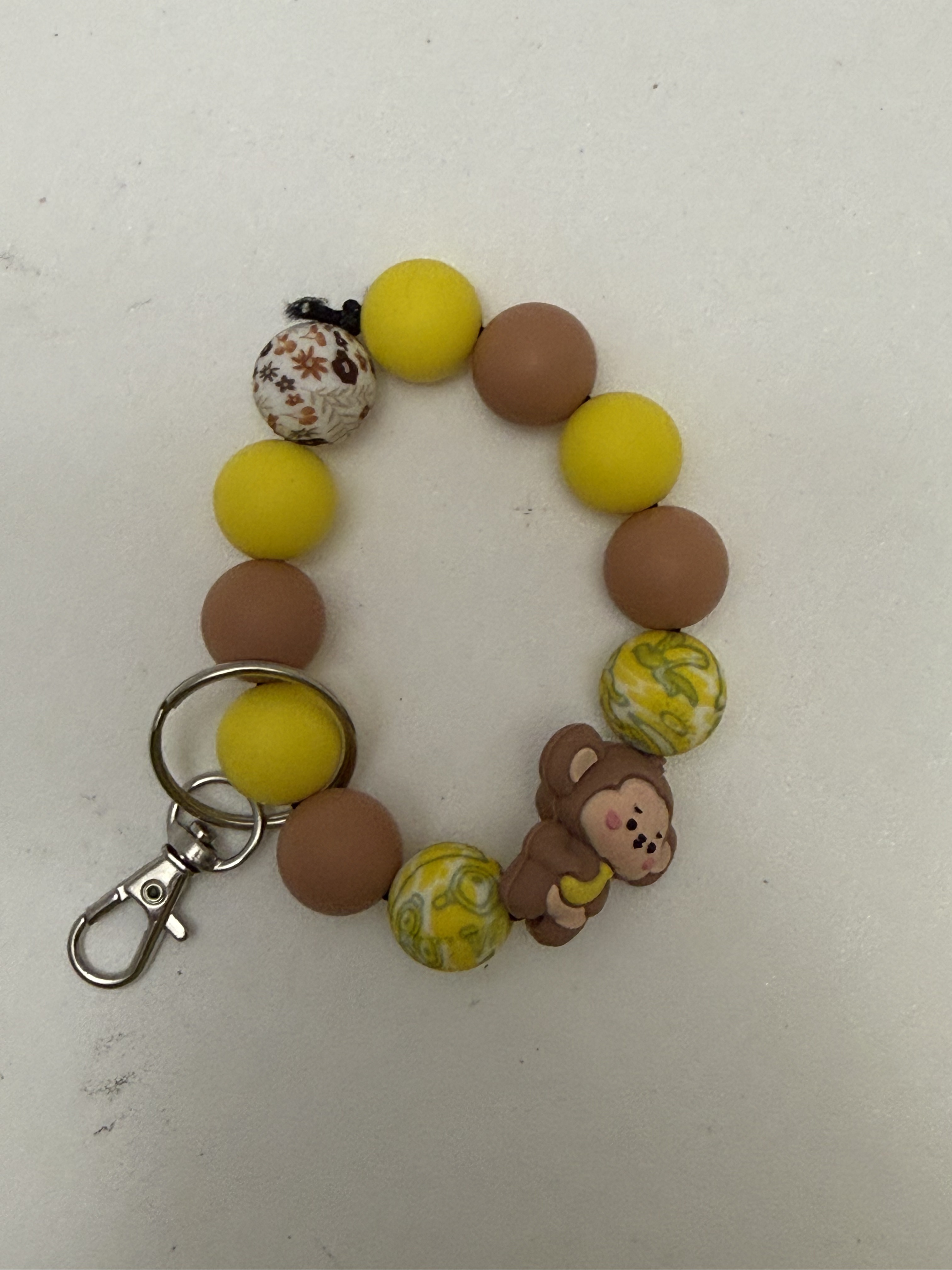 Beaded wristlet keychain with kawaii monkey figure, yellow and brown beads, banana-print rounds, and silver swivel clasp