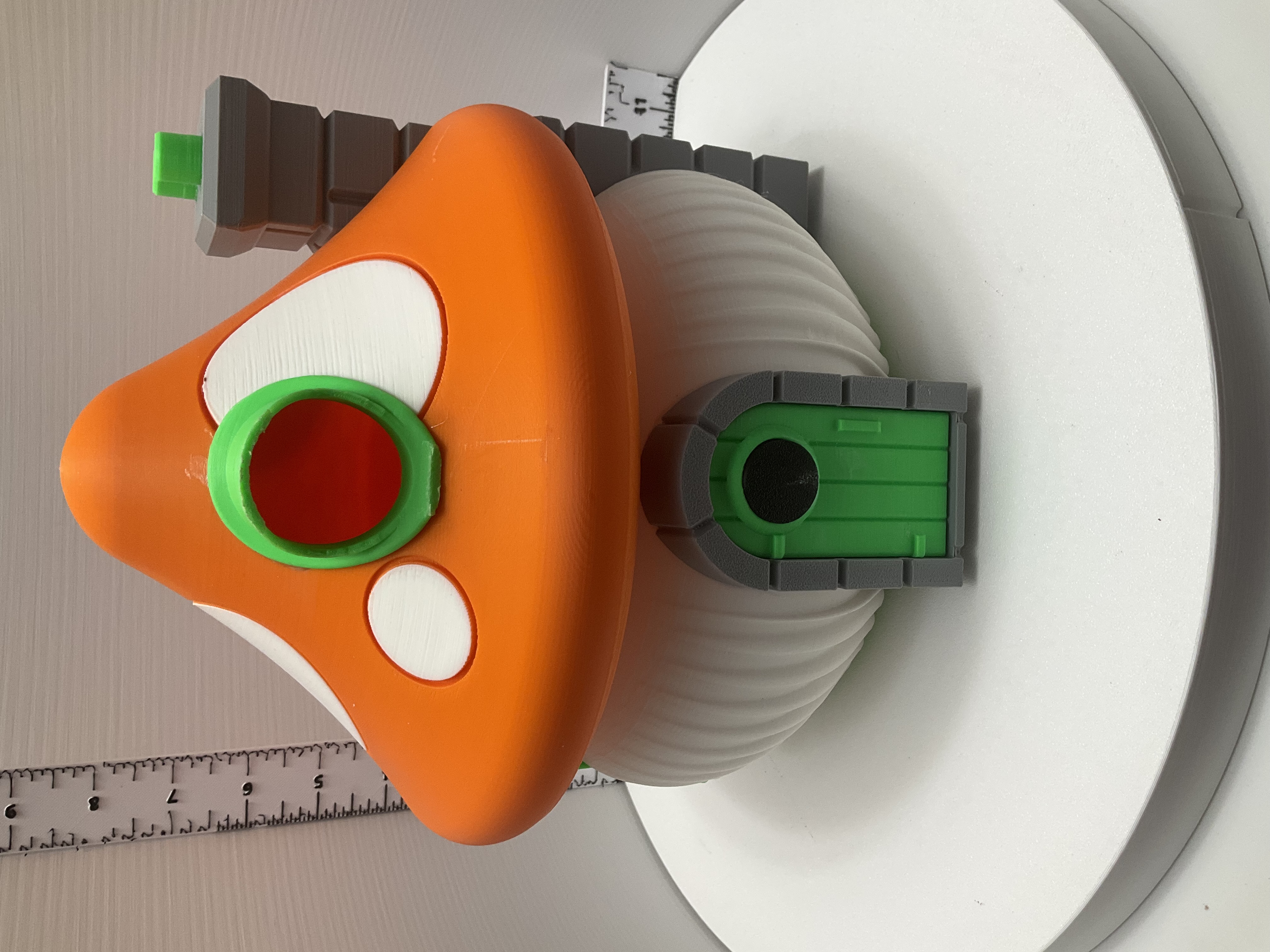 Orange mushroom-cap birdhouse with green door, white spots, and stacked-stone chimney detail