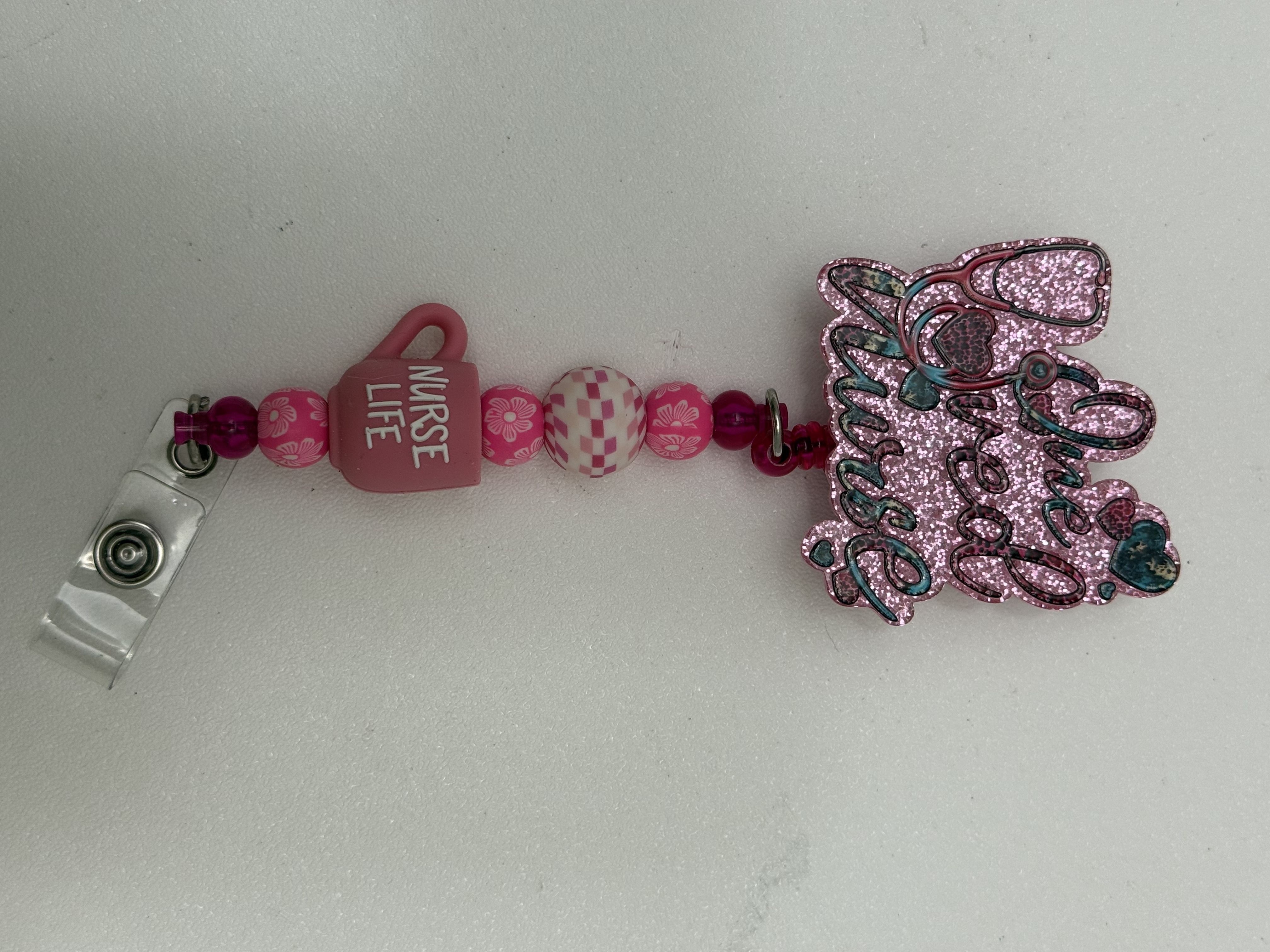 Pink beaded badge reel with nurse life mug charm and glitter pendant on white background