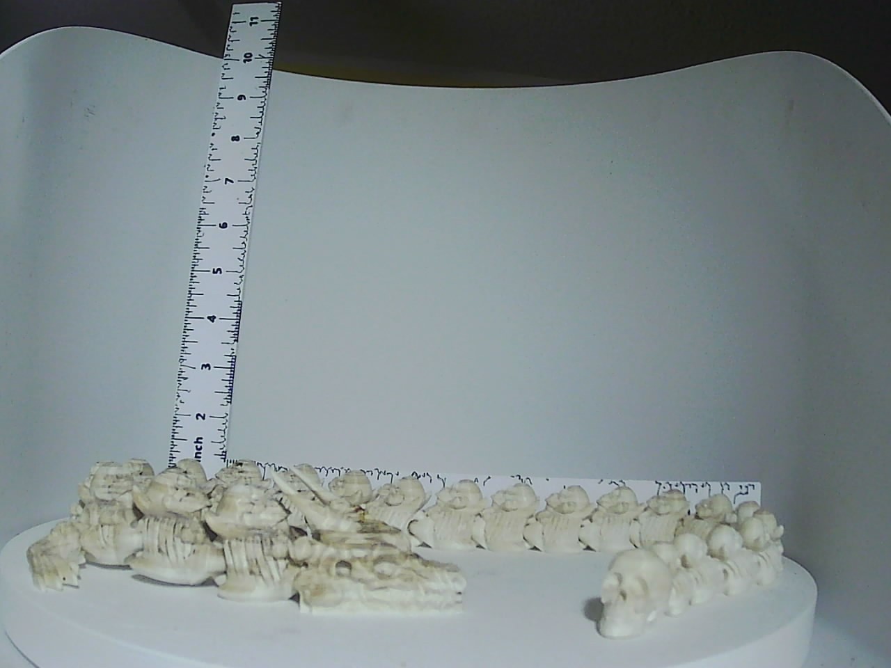 White 3D printed skeletal creature miniatures grouped together on a white display surface next to a ruler for scale
