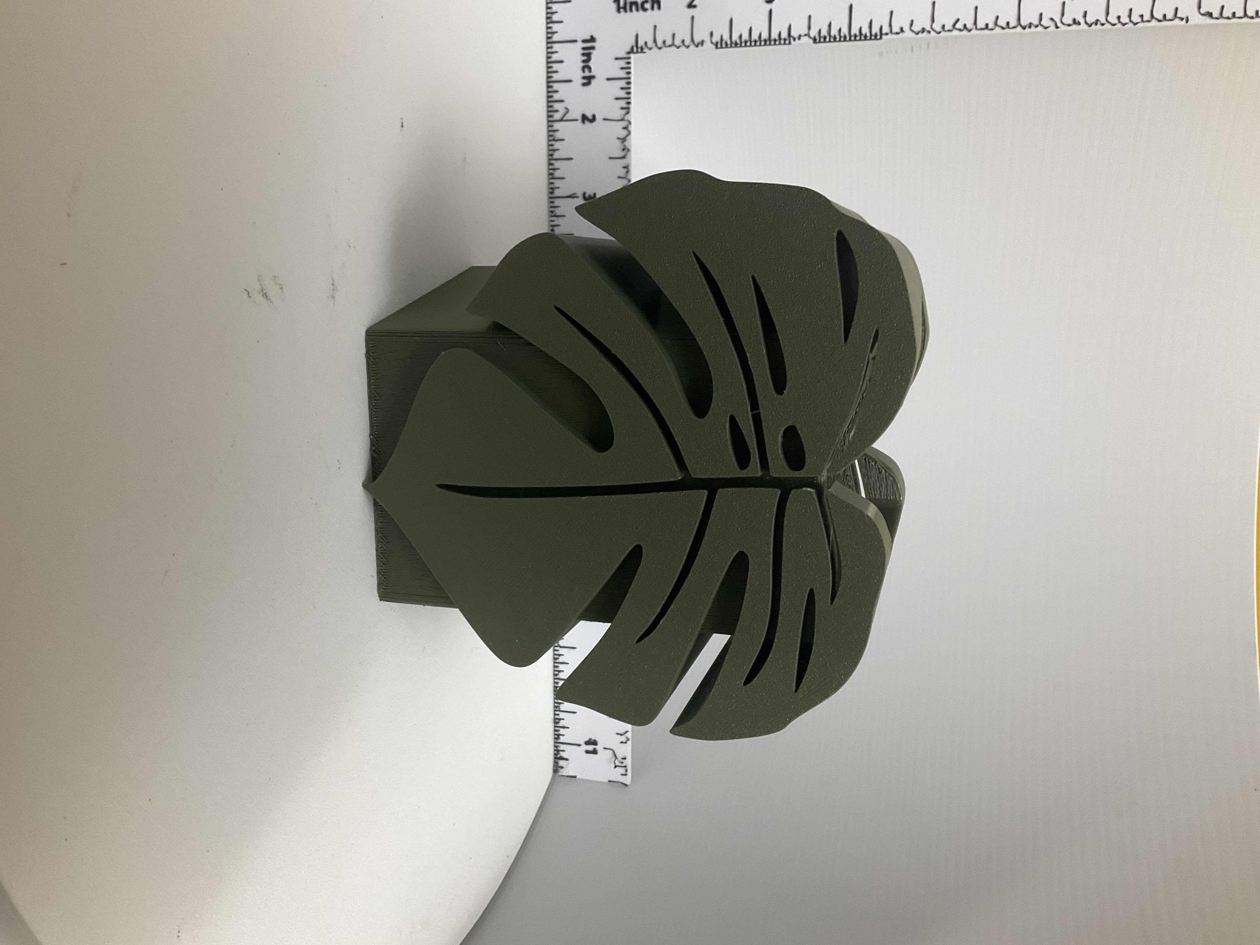 Olive green 3D printed monstera leaf planter with cutout details on geometric base