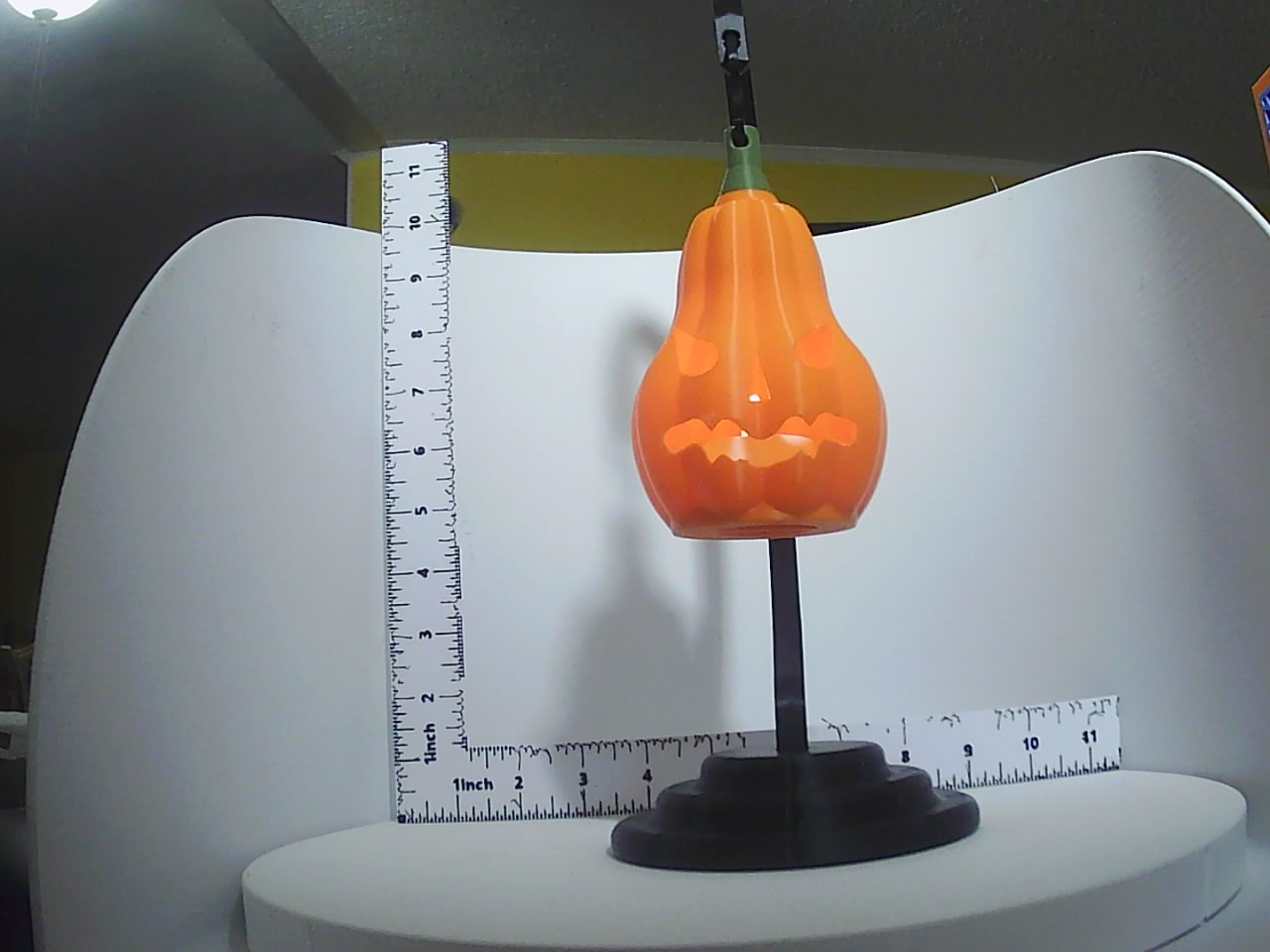 Orange pear-shaped jack-o-lantern candle holder on dark pedestal stand with ruler for scale