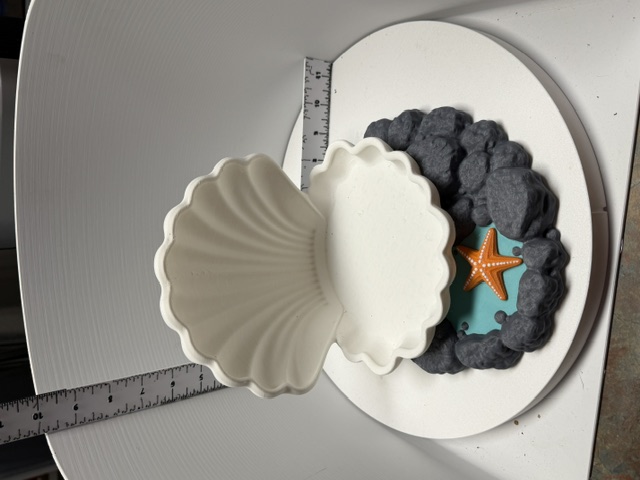 White open scallop shell dish on a grey rocky base with orange starfish and teal accent