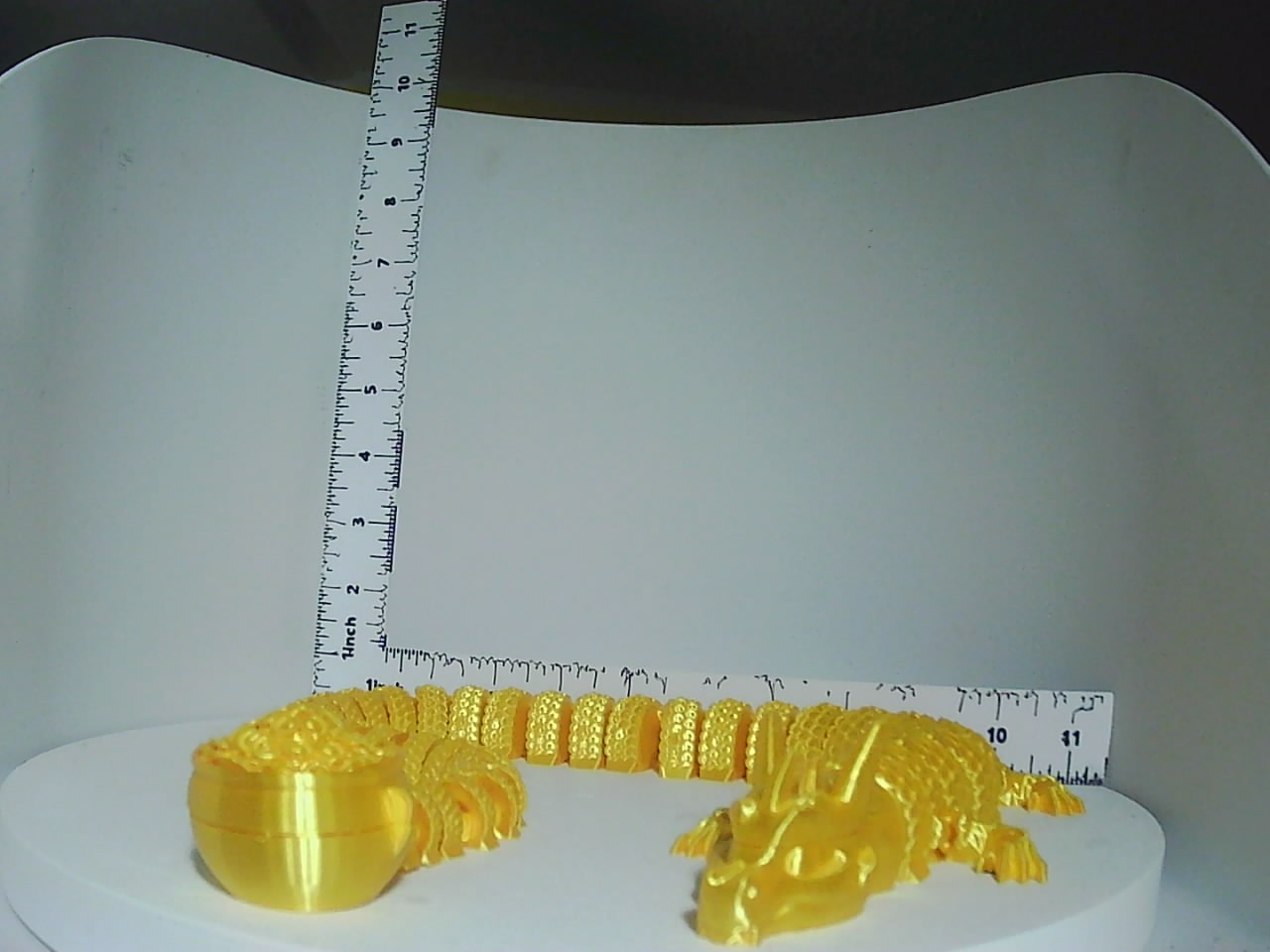 Golden articulated dragon with scaly segments and orb tail shown beside ruler for scale