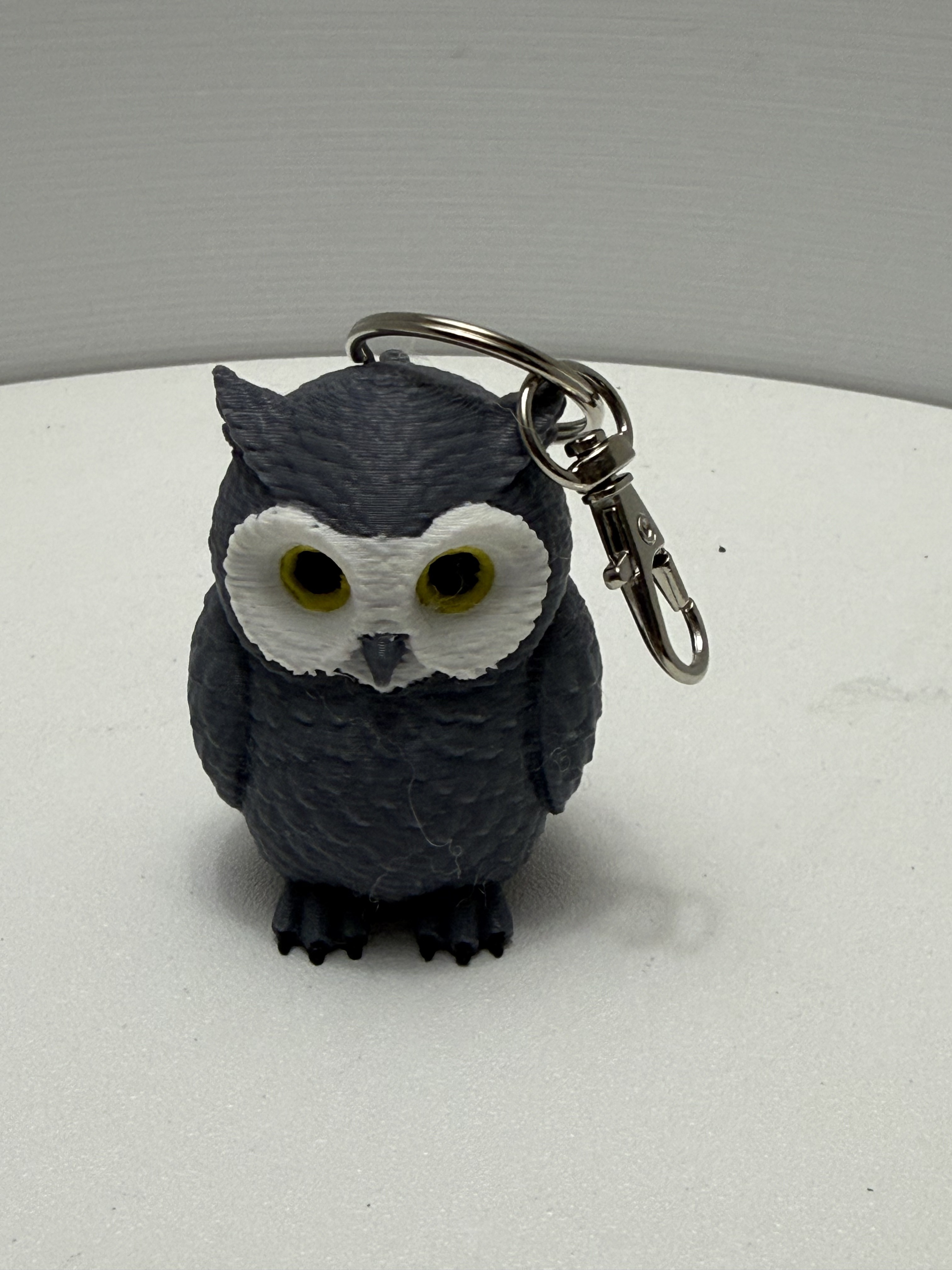 Dark slate owl keychain with golden eyes and silver swivel lobster clasp on white surface