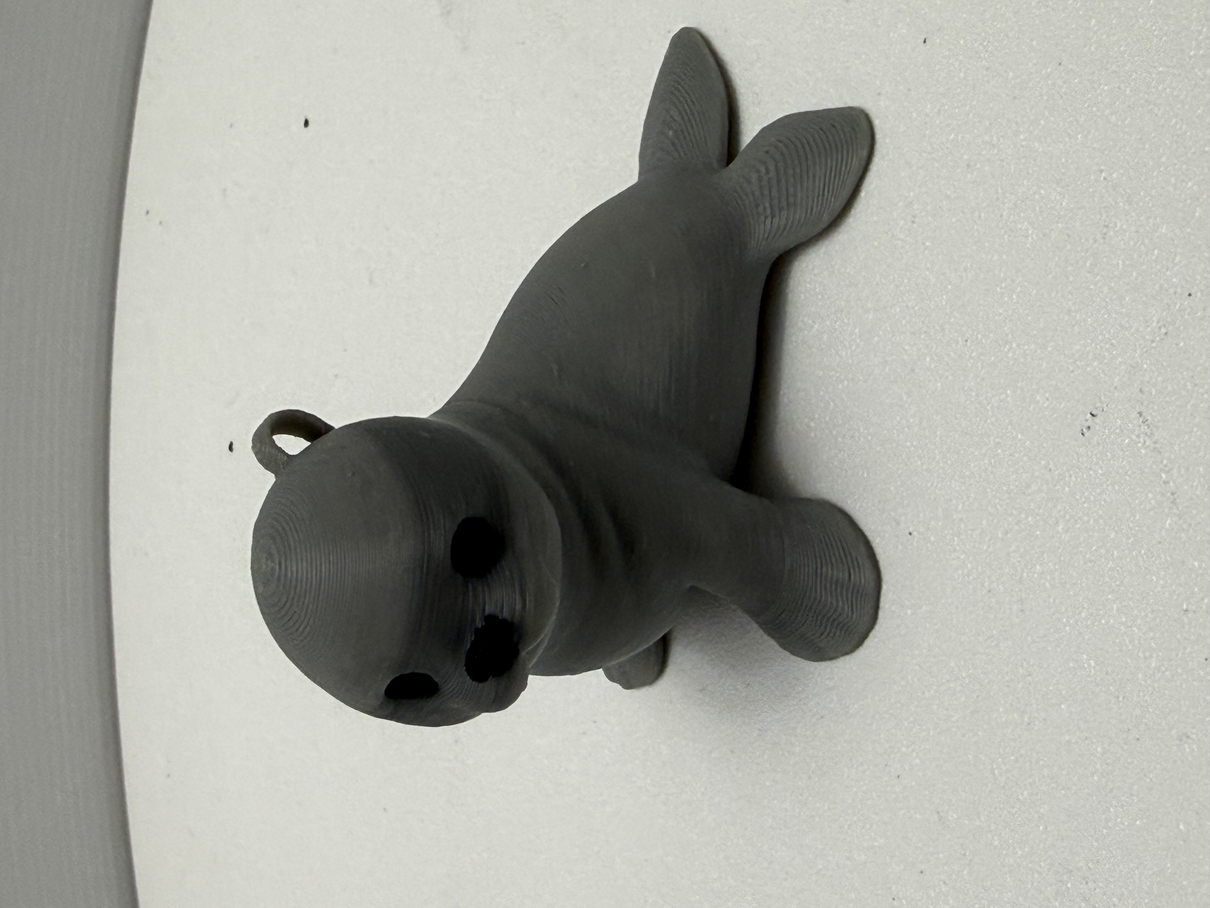 Slate grey 3D printed seal figurine with hanging loop sitting on white surface