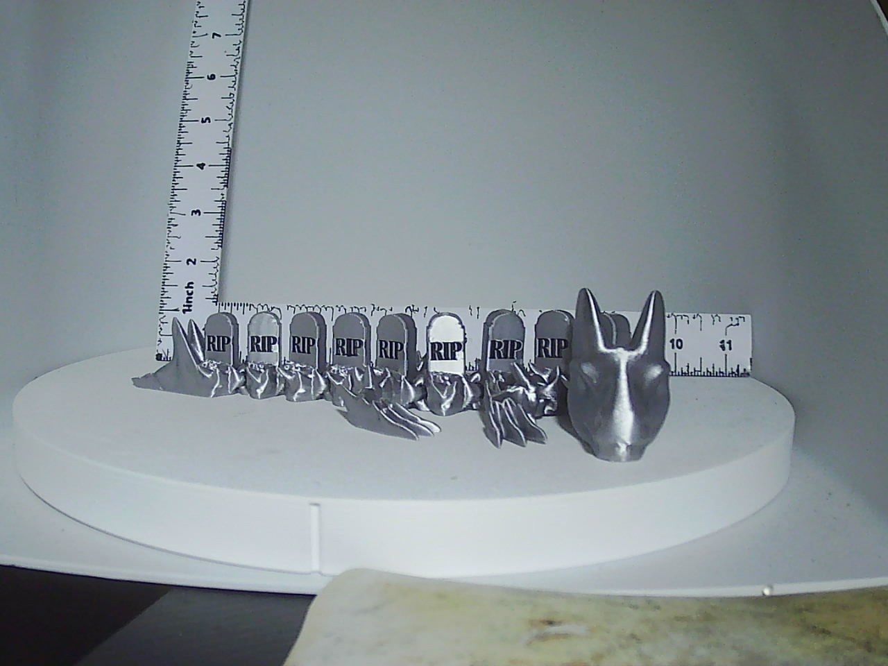 Silver 3D printed graveyard creature with RIP tombstones and horned head shown beside ruler for scale