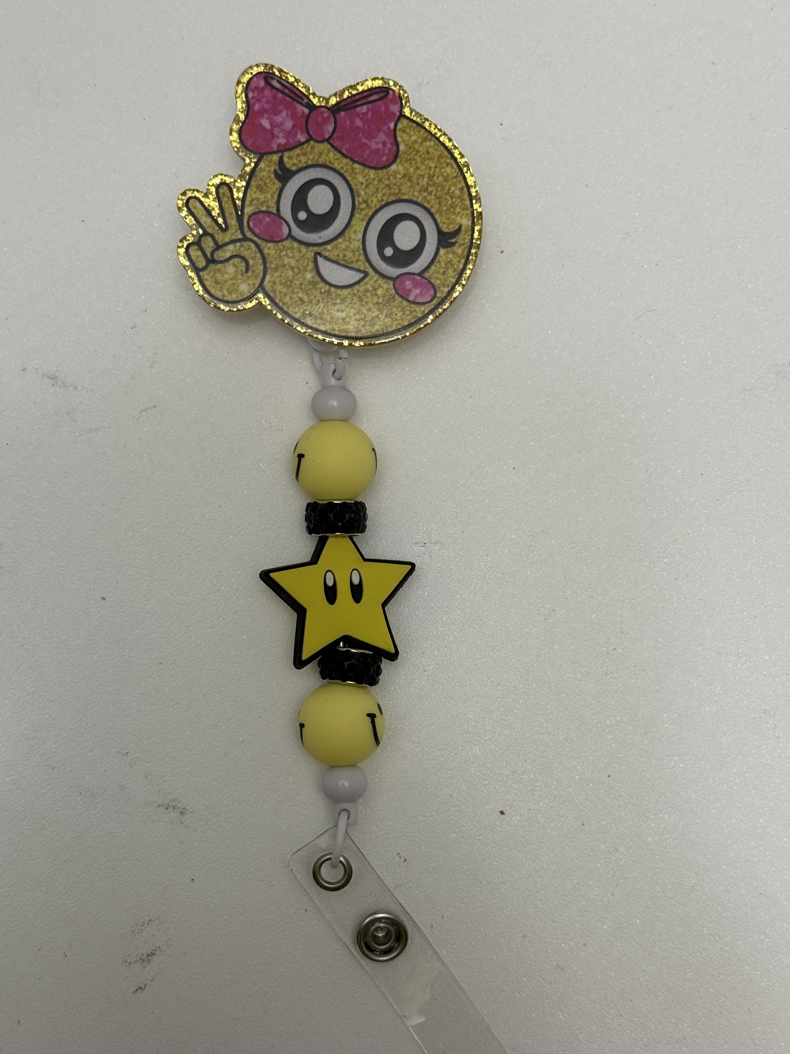 Gold glitter kawaii girl badge reel with pink bow, yellow beads, and smiling star charm