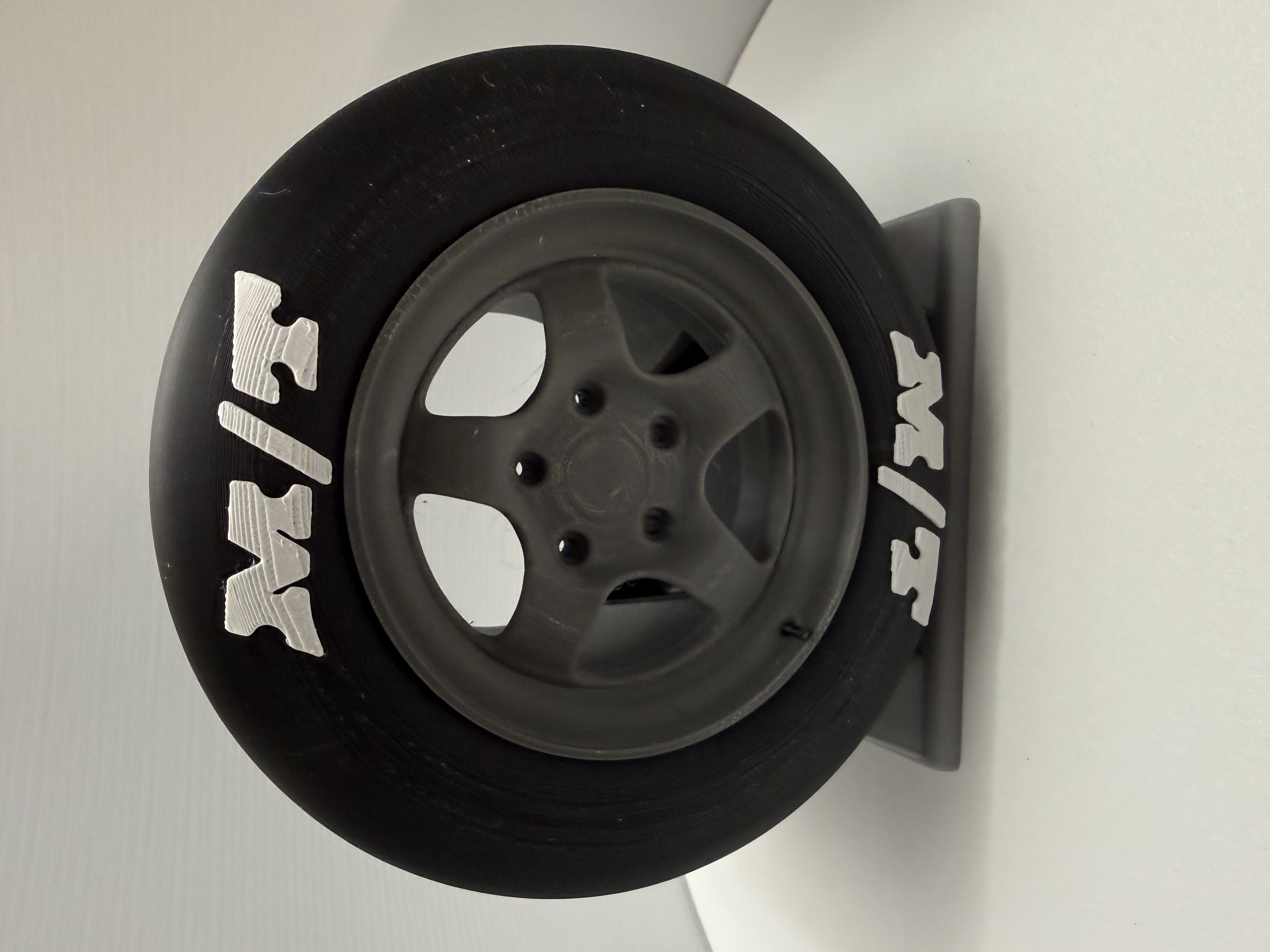 3D-printed drag slick wheel model upright on matching gray display stand against white background