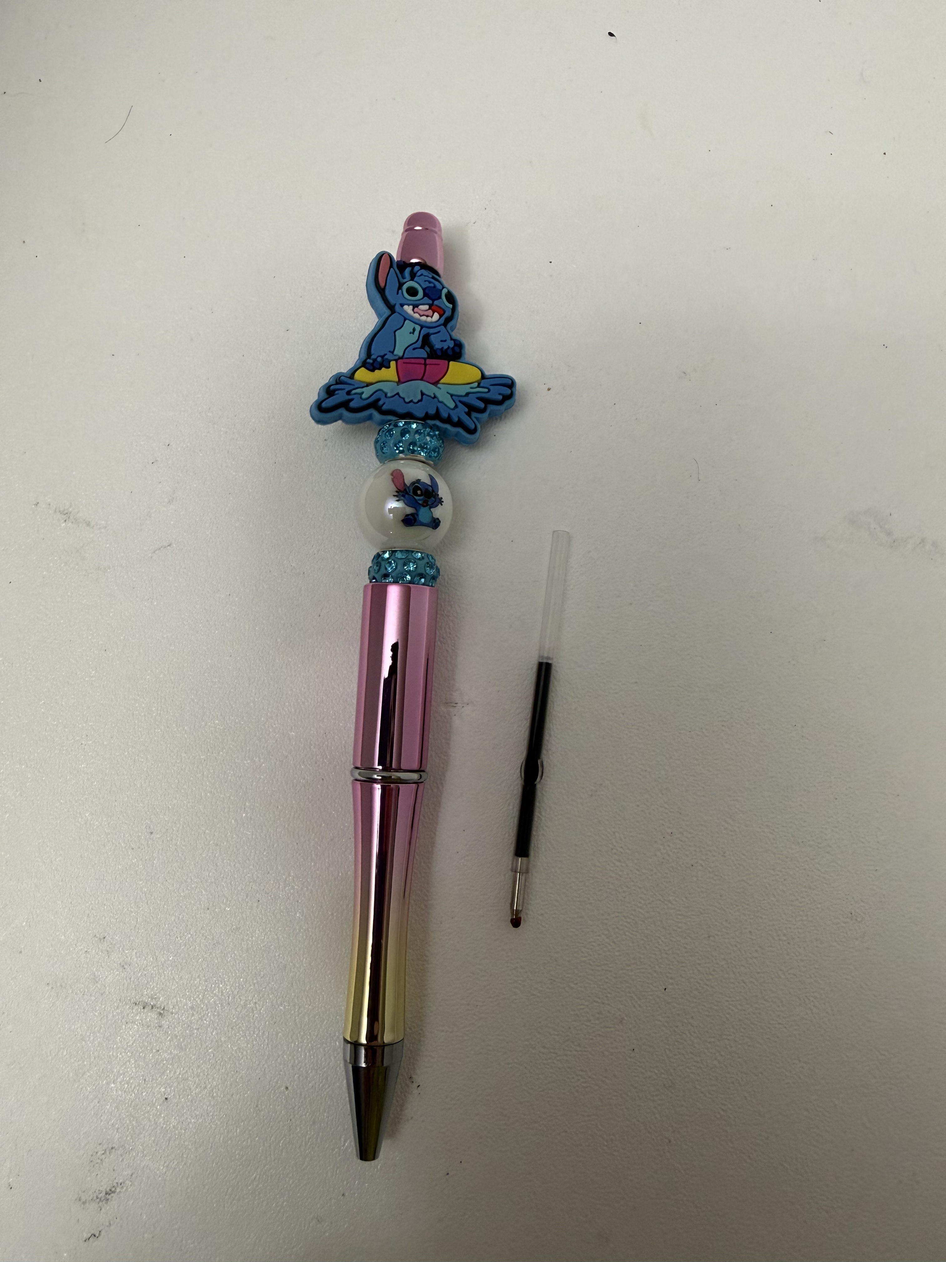 Pink metallic ballpoint pen with blue character charm topper and aqua rhinestone beads