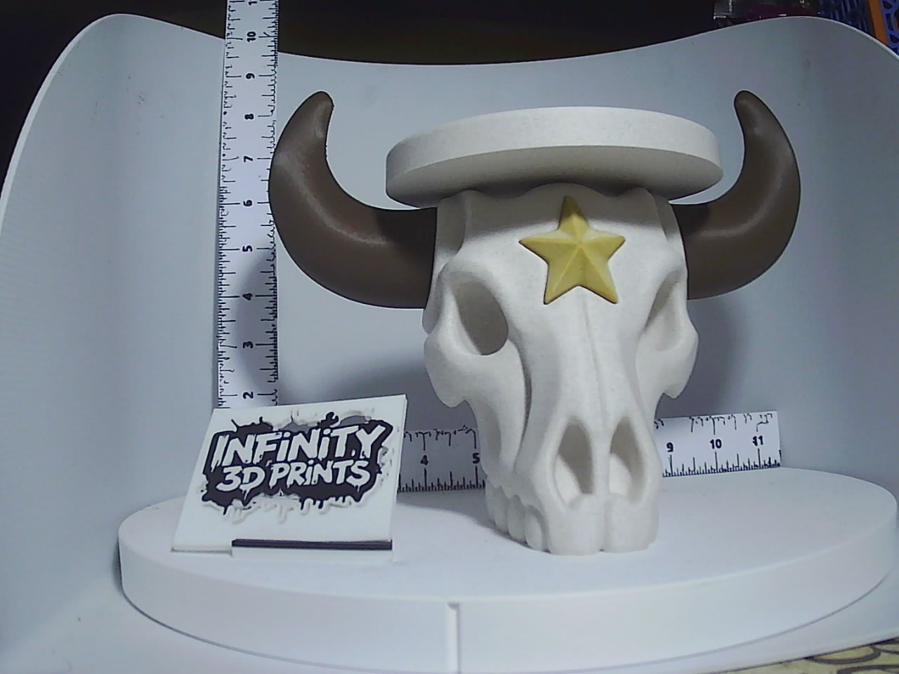 White 3D printed bull skull candle holder with brown horns and gold star accent shown next to a ruler for scale