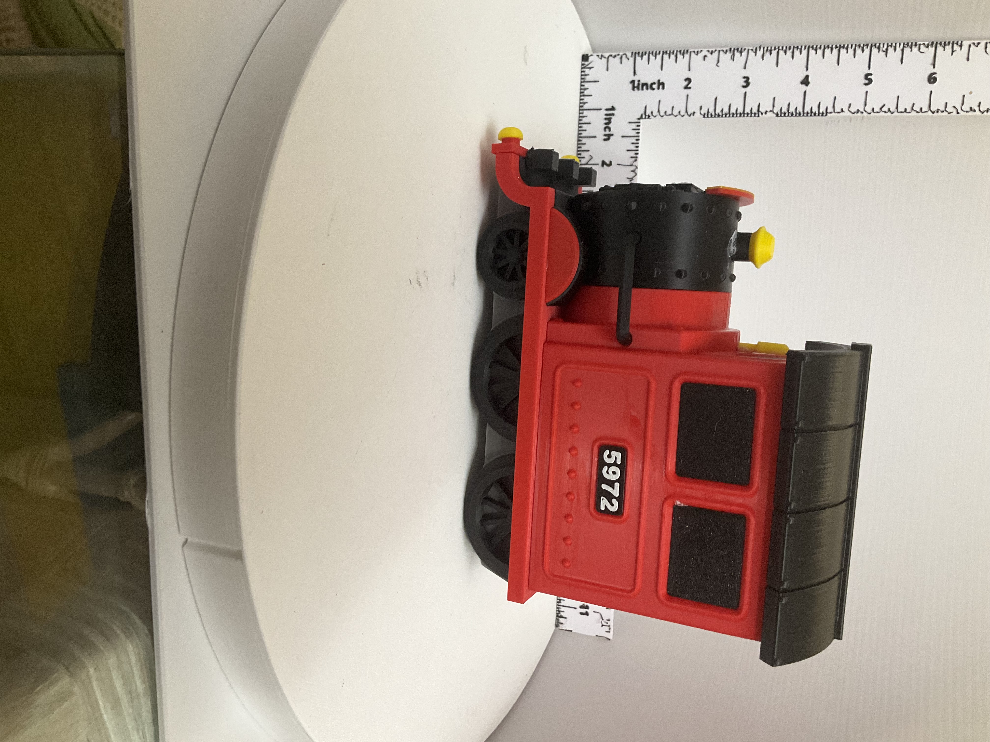 Side view of red steam locomotive coin bank showing spoked wheels and ribbed dark roof