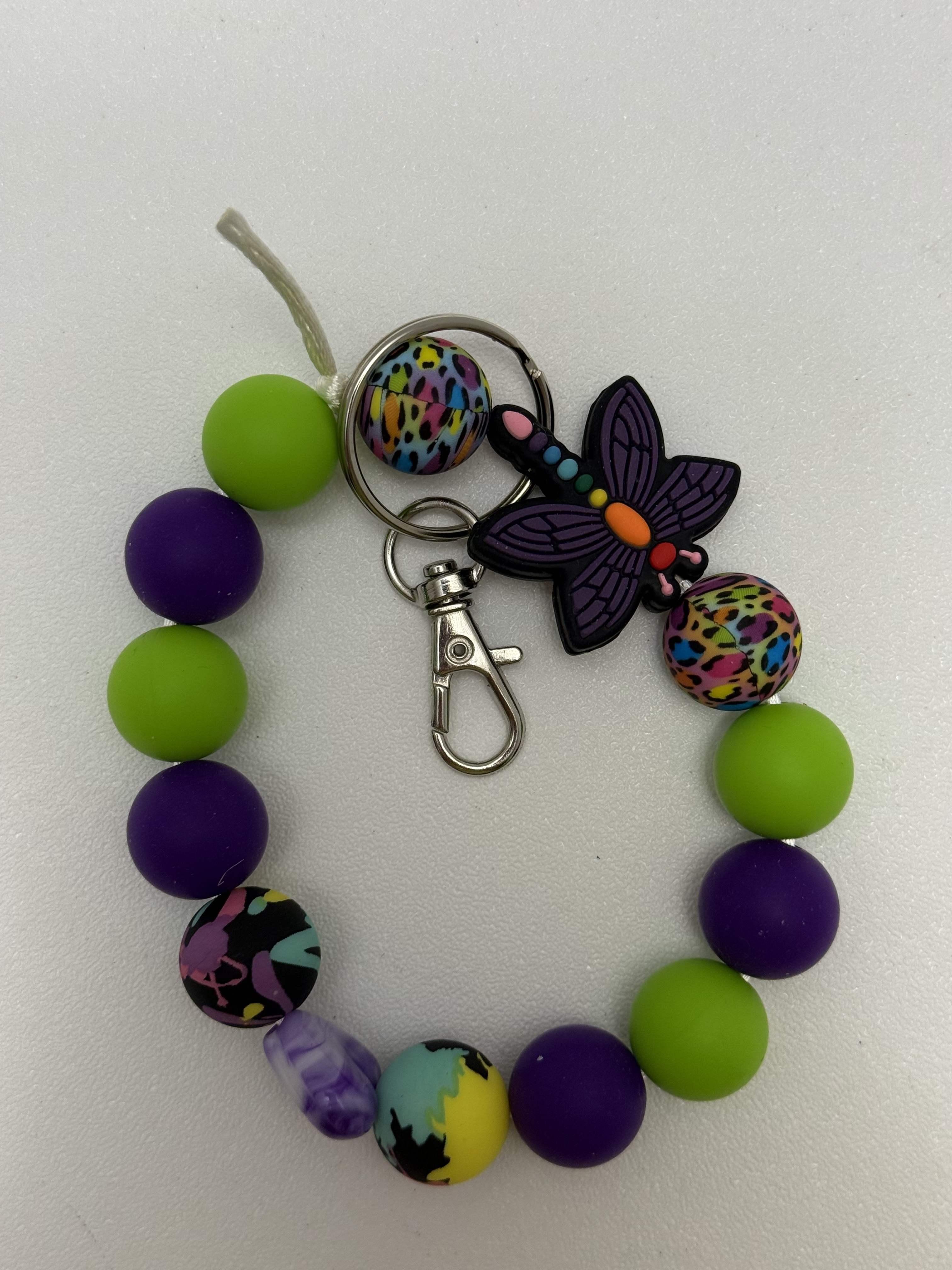 Beaded wristlet keychain with lime green and purple beads, patterned accent beads, and a purple rubber butterfly charm on a silver-tone clasp