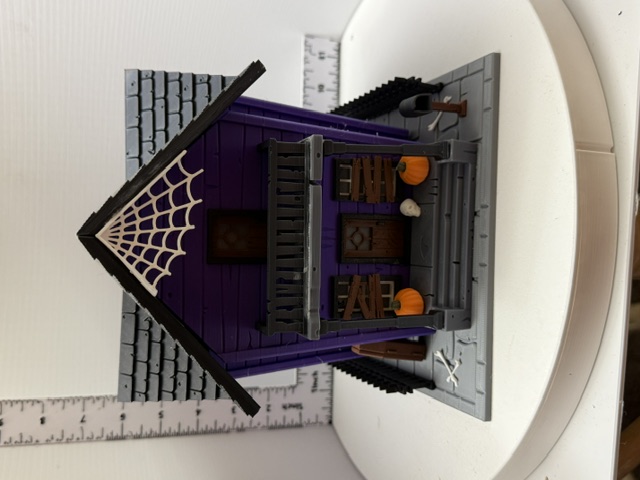 Front view of purple 3D-printed haunted house with spiderweb gable, orange pumpkins, and grey shingled roof