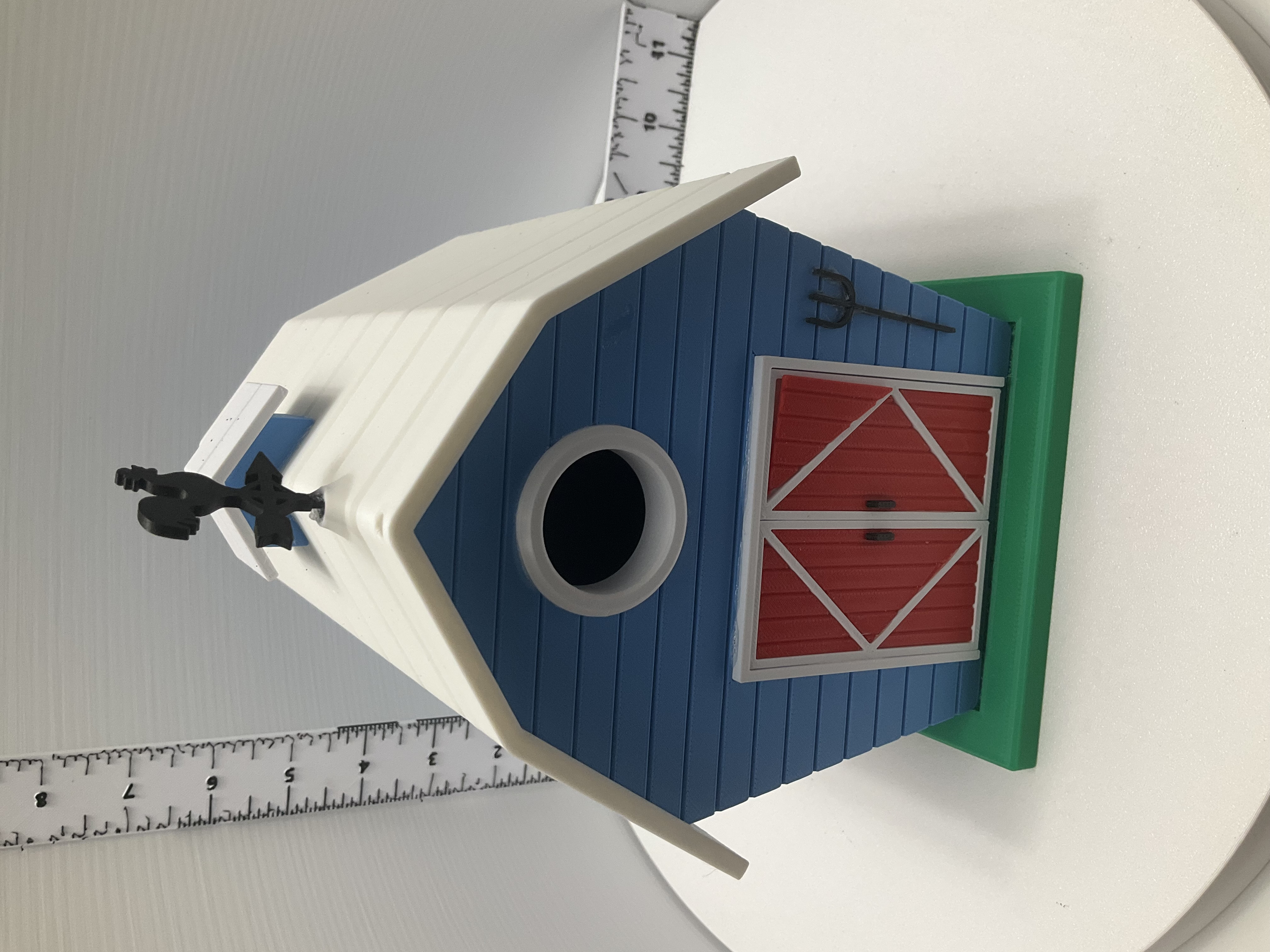 Blue barn birdhouse front view showing round entry hole, red barn doors, pitchfork detail, and rooster weathervane