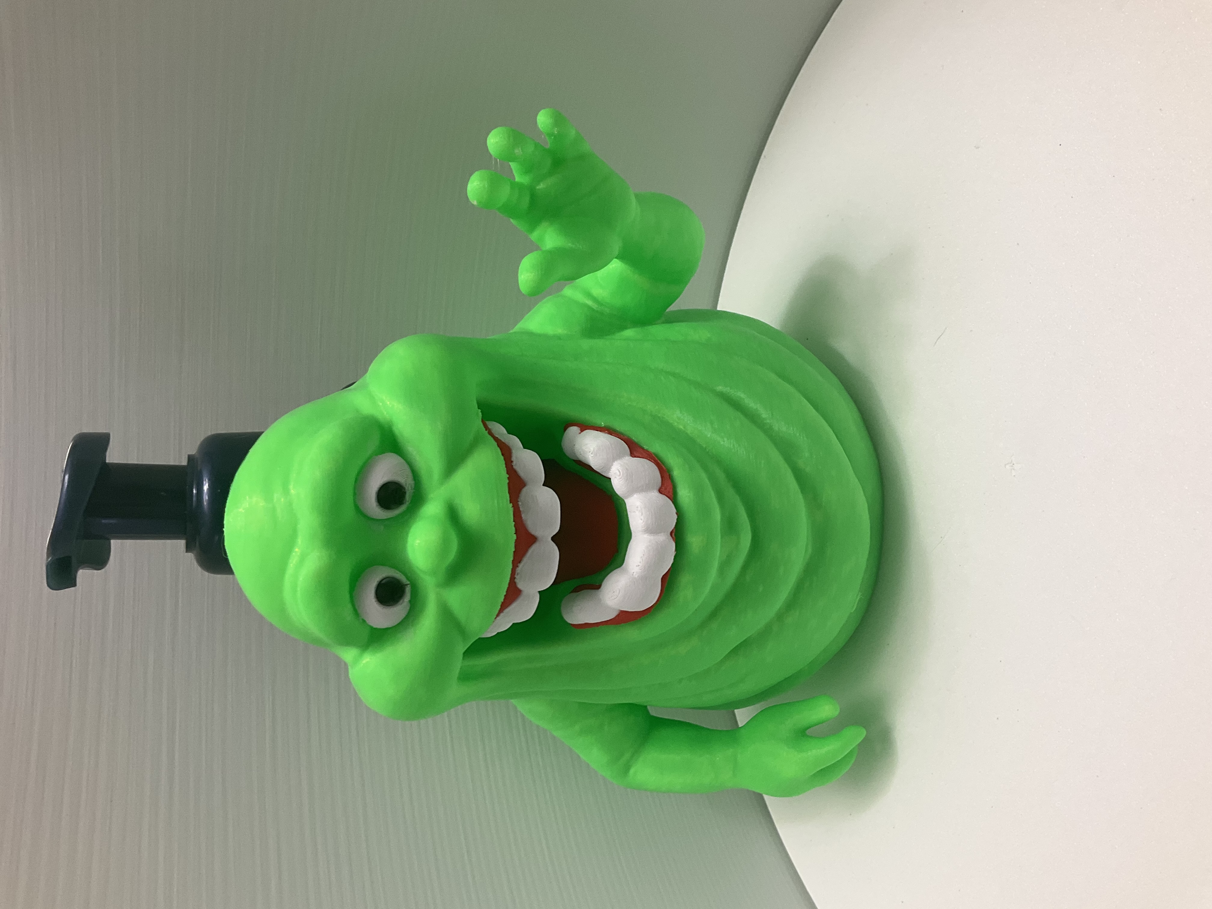 Bright green ghost soap dispenser with grinning mouth and waving hand on white surface