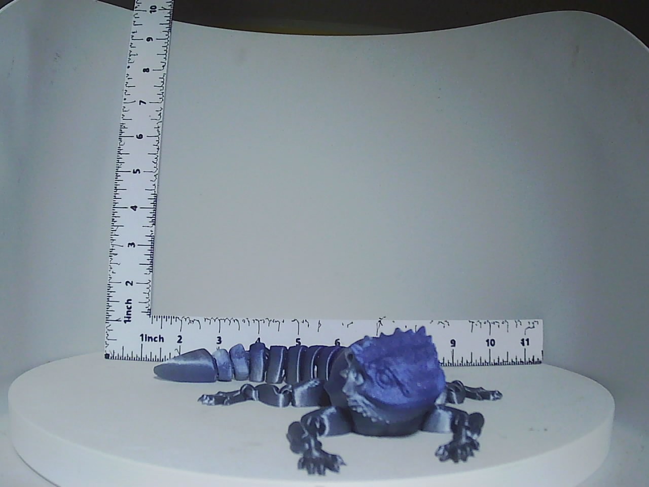 Blue-violet articulated 3D printed bearded dragon displayed beside a ruler for scale