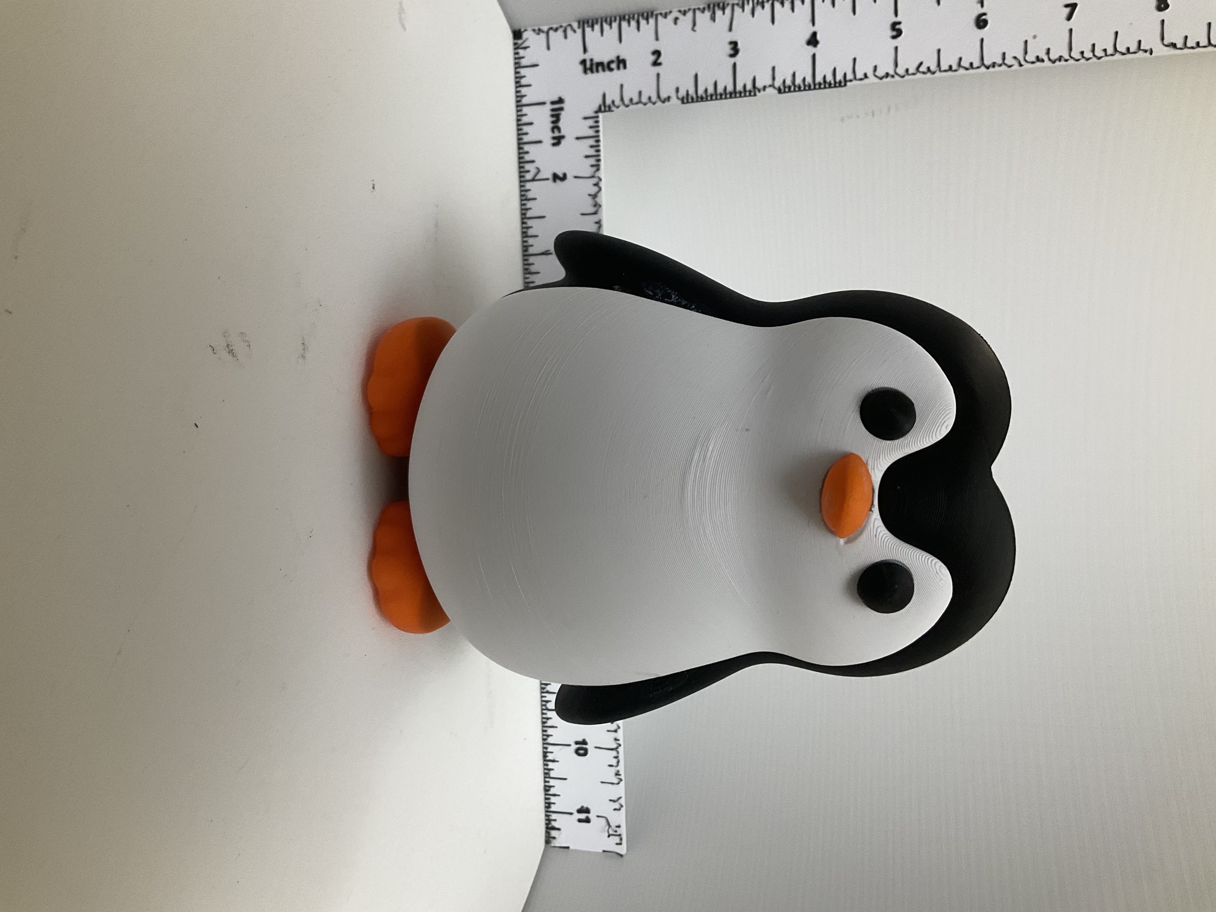 Front view of a round 3D printed penguin figurine with orange feet and beak