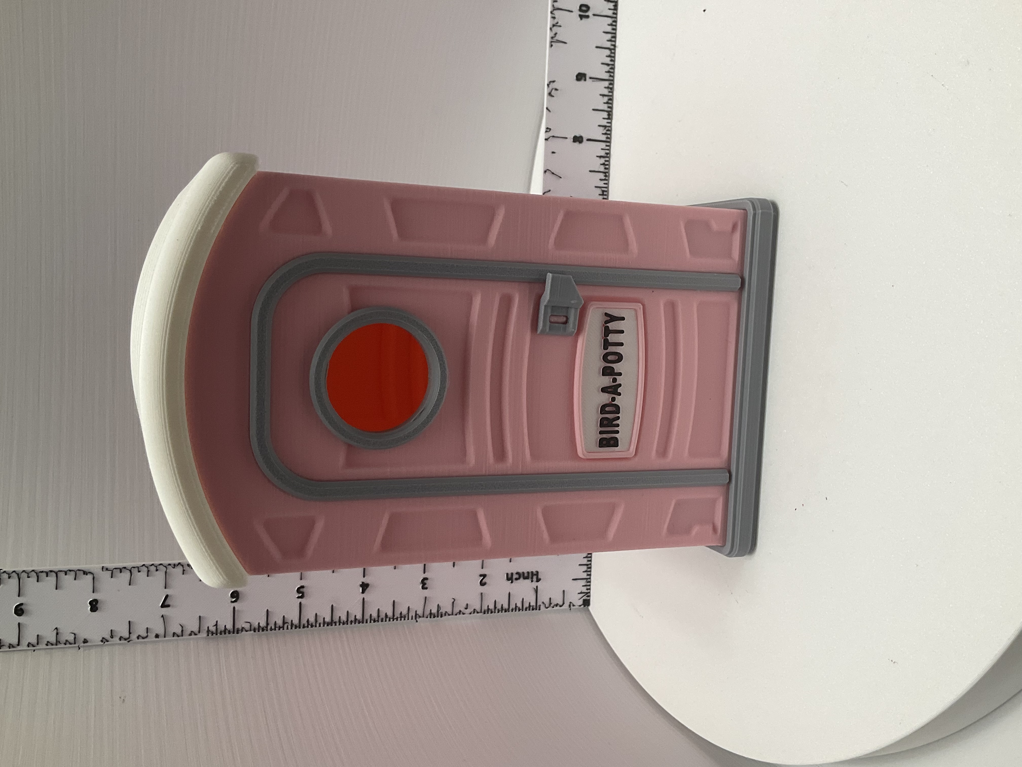 Pink 3D-printed miniature porta-potty labeled Bird-A-Potty with white roof and red circle window