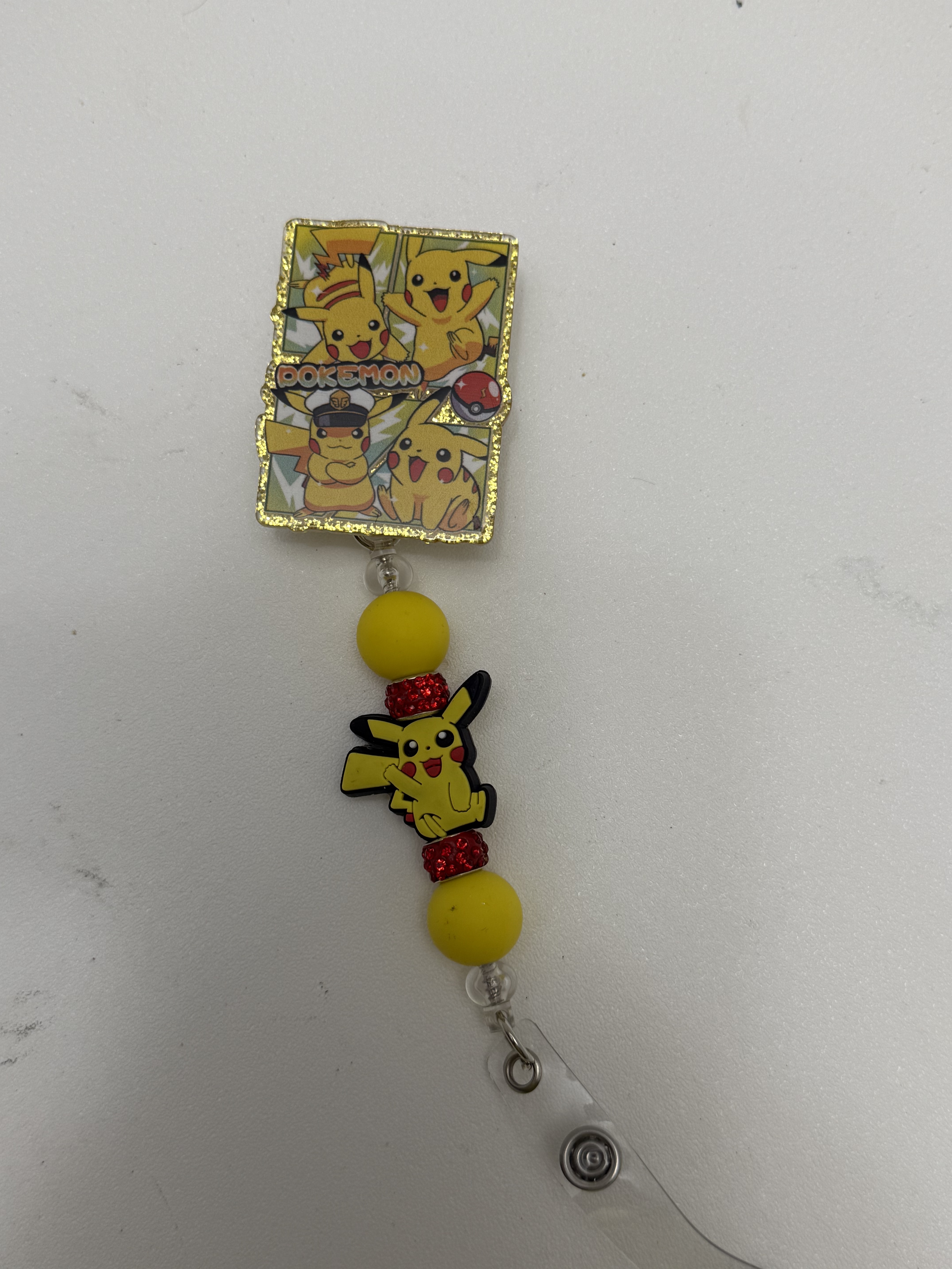 Retractable badge reel with gold comic-panel charm, yellow beads, red rhinestone barrels, and kawaii character focal