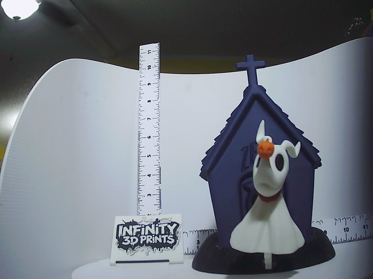 White ghost-dog figurine with orange pumpkin and navy gravestone base displayed with ruler for scale