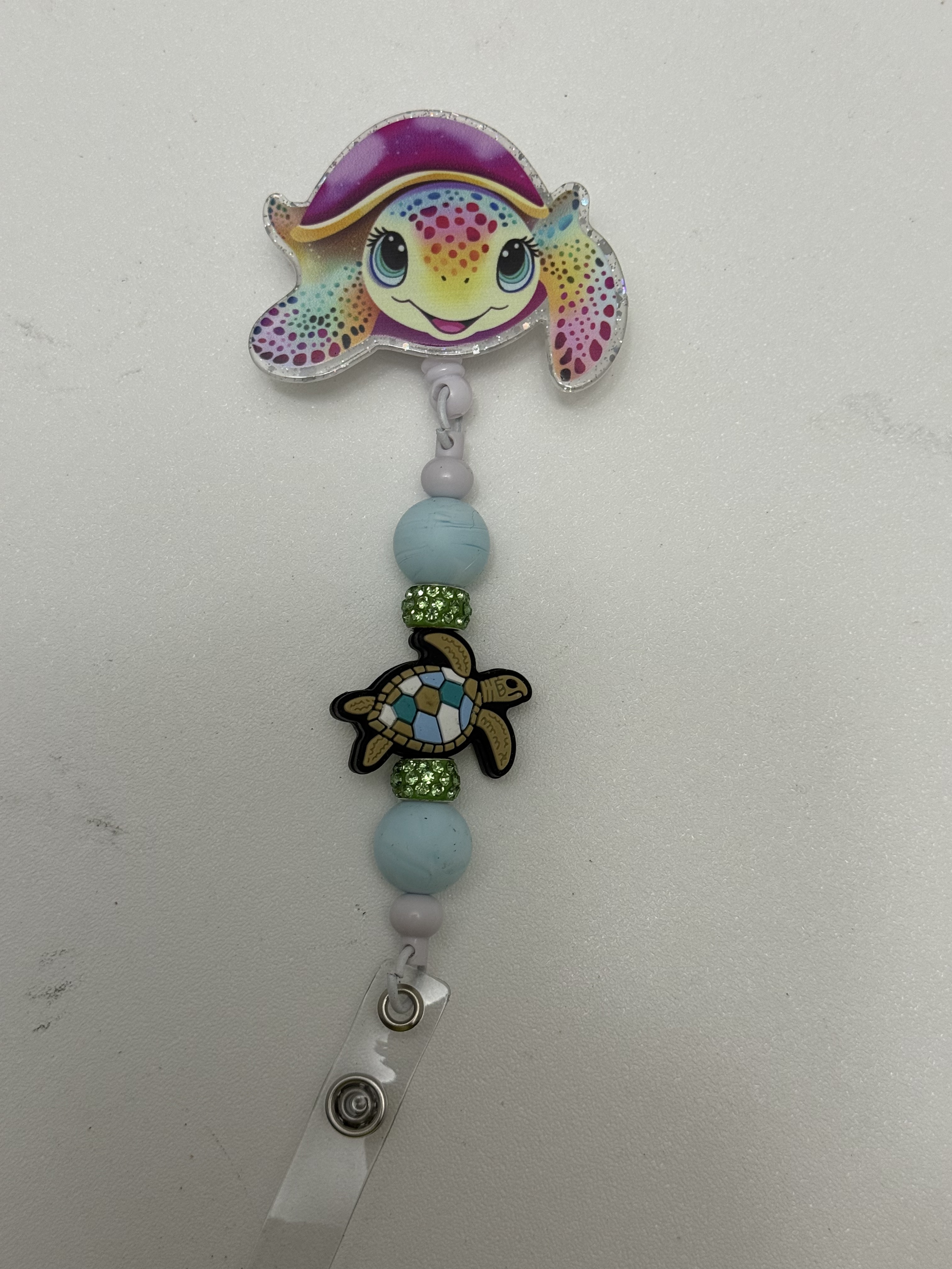 Retractable badge reel with glittery rainbow fish topper, blue beads, green rhinestone rings, and mosaic sea turtle charm