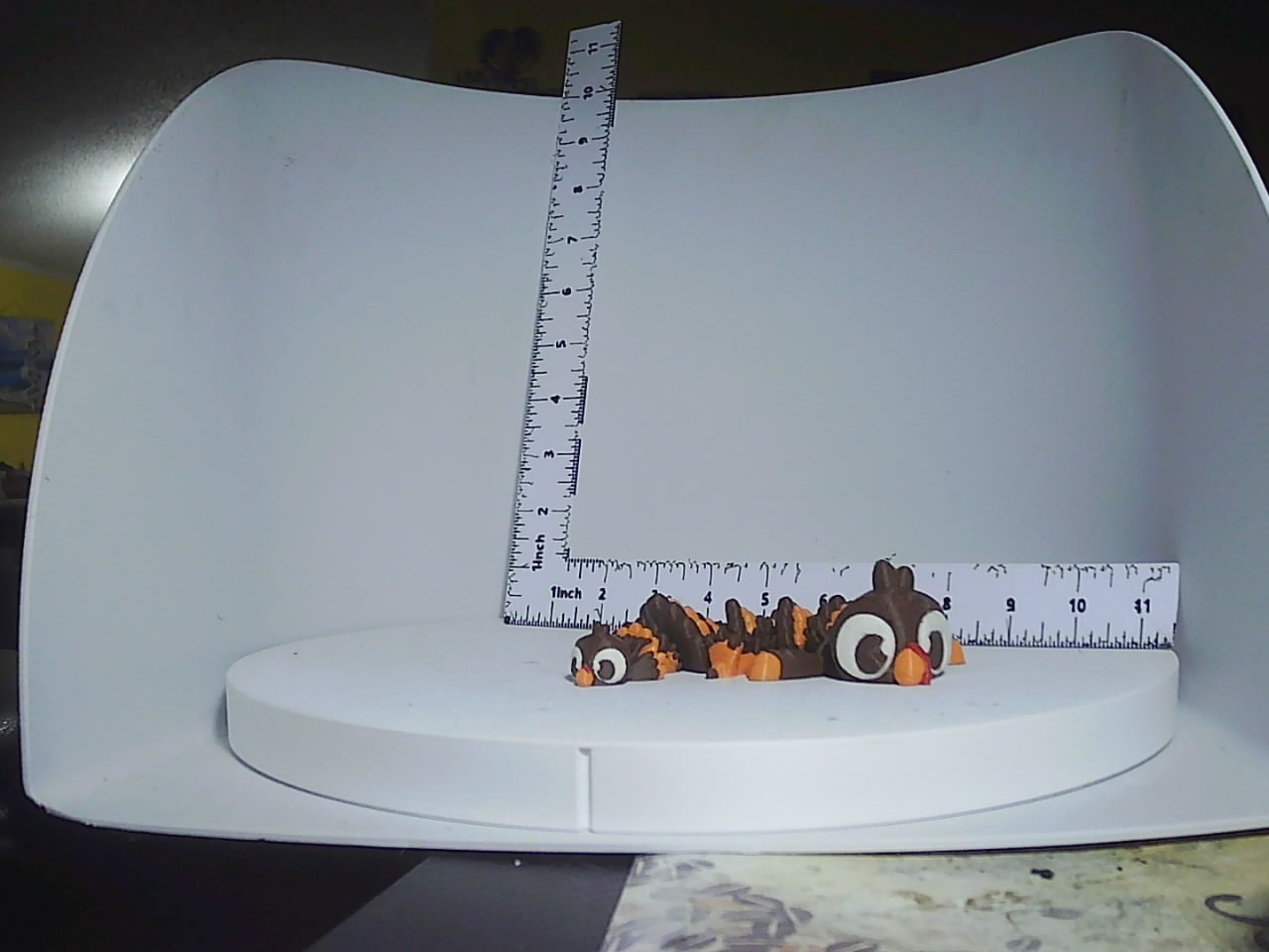 Small brown and orange turkey figurine peeking over a ruler on a white display stand