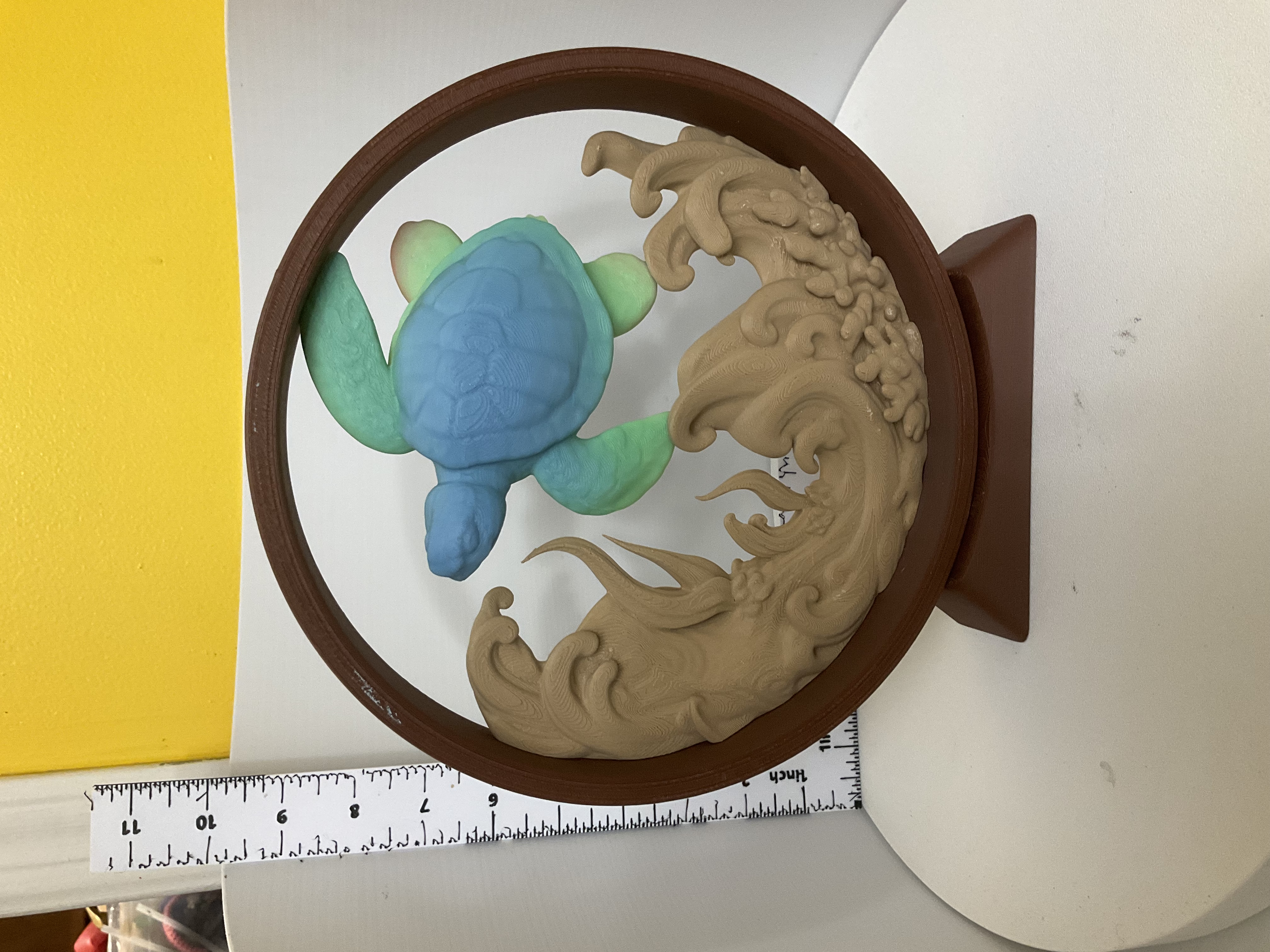 3D printed circular display with blue-green sea turtle above sandy-toned sculpted waves