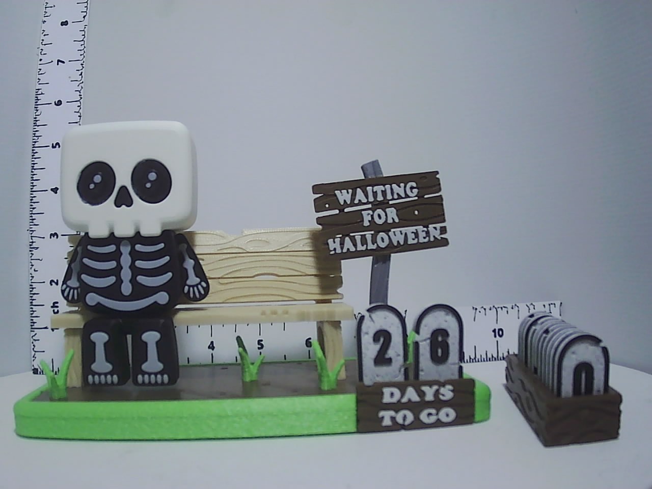 Printed skeleton figure on bench beside a Waiting for Halloween sign and tombstone day-countdown tile holder