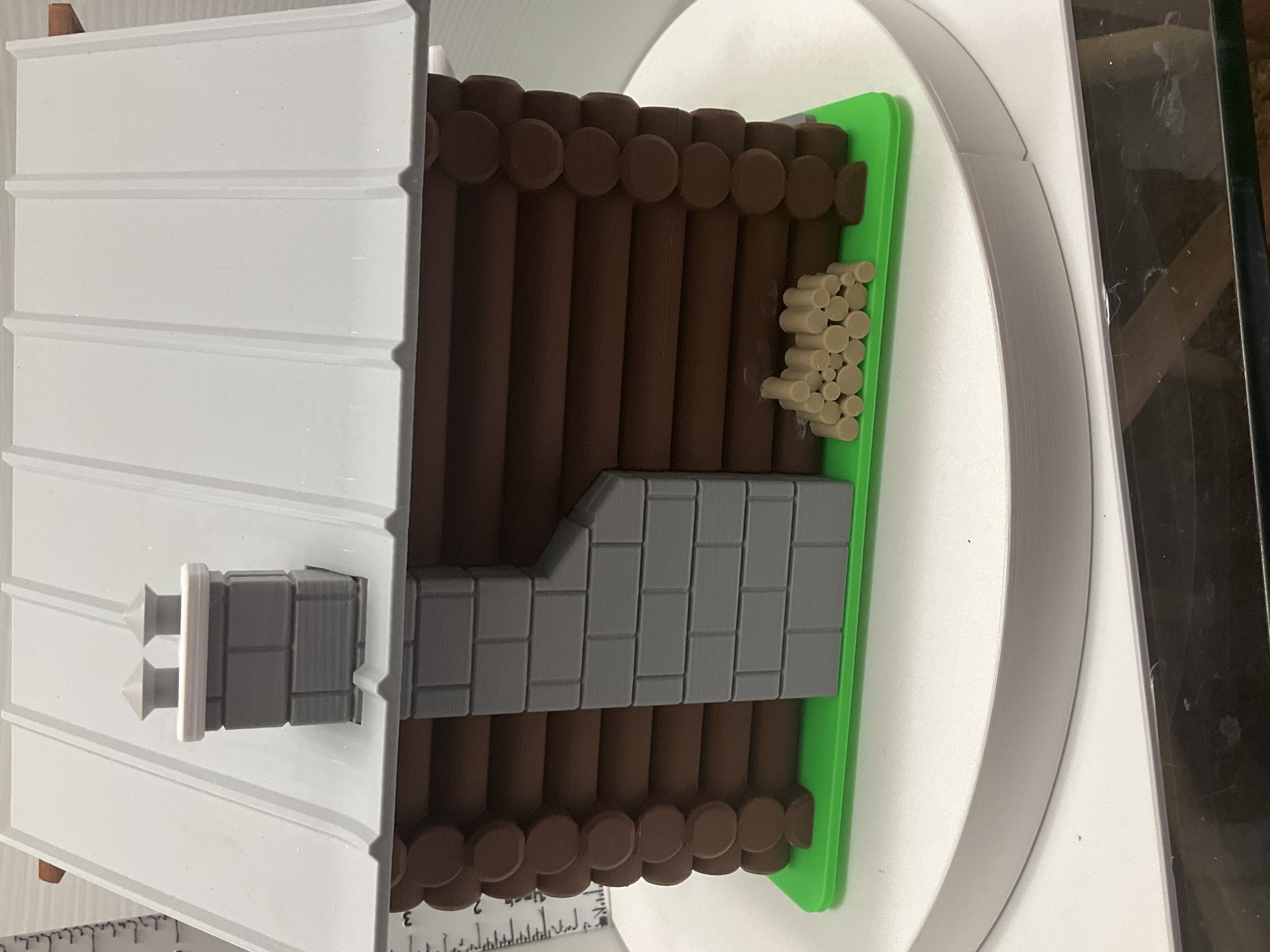 Side and rear view of log cabin miniature showing stone chimney and stacked firewood on green base