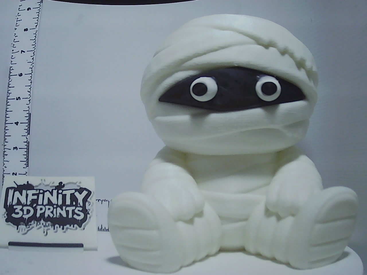 Chubby seated mummy figurine with bandage wraps and wide cartoon eyes on white surface