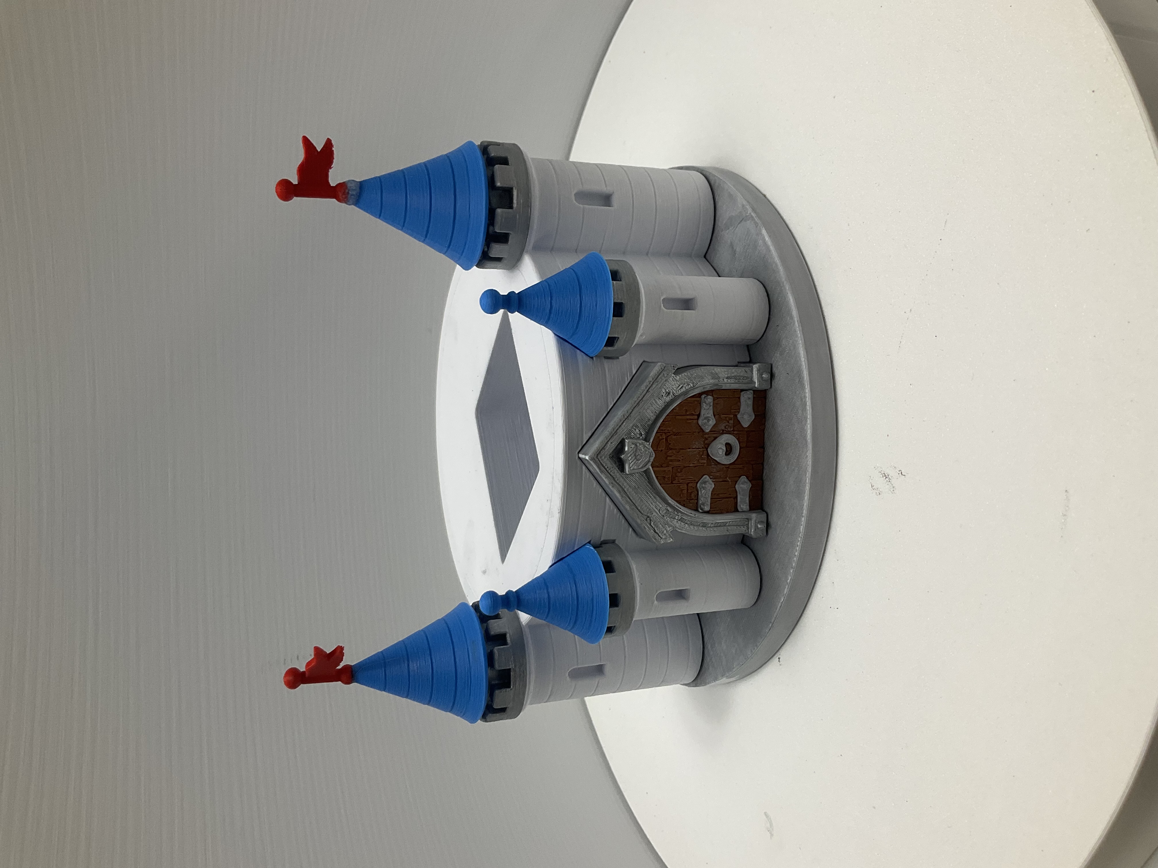 3D-printed castle soap dispenser holder with blue spires, red flags, and brown arched door