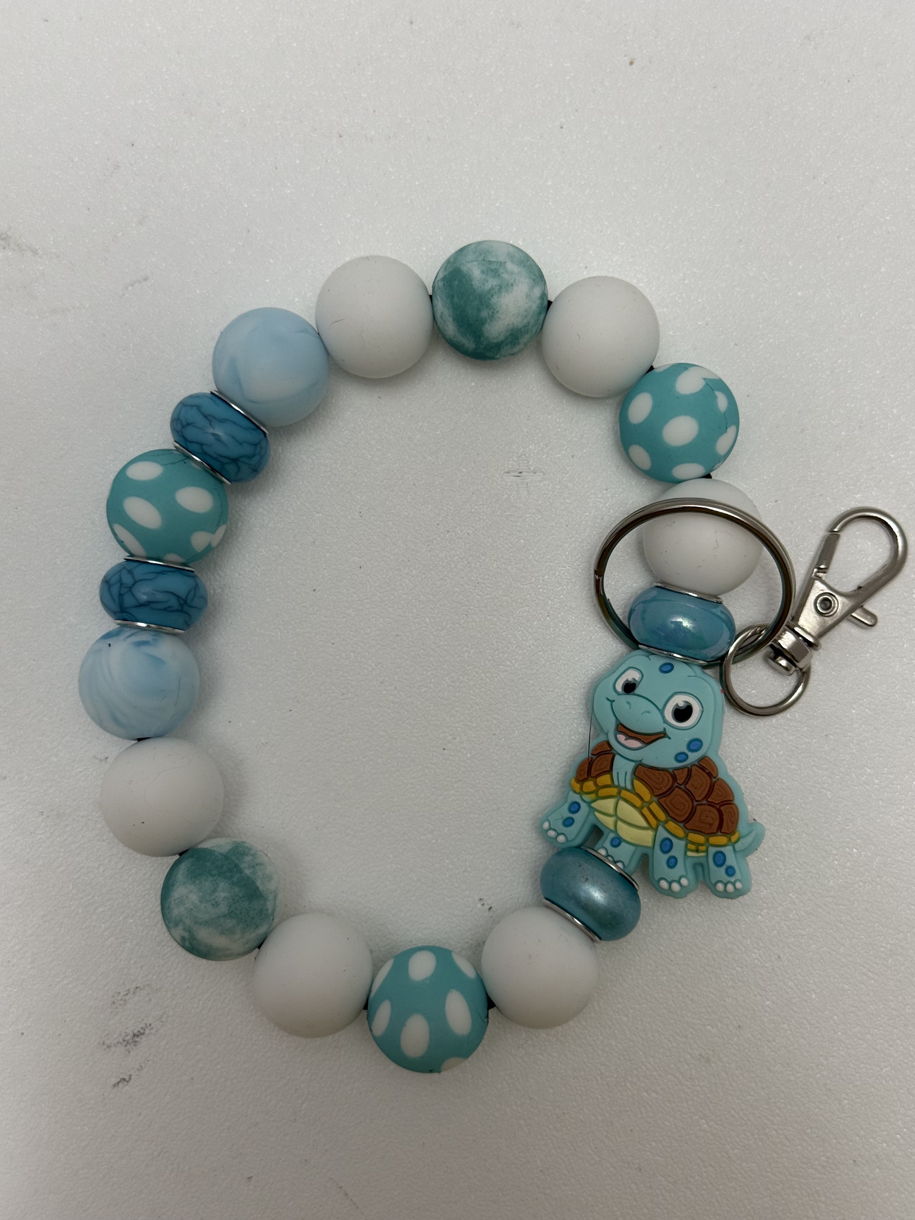 Beaded wristlet keychain in teal and white with smiling cartoon turtle charm and silver clasp