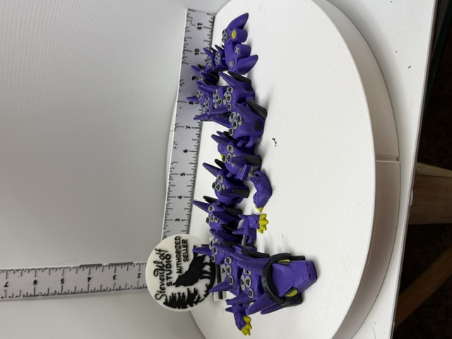 Purple articulated game controller dragon coiled on white surface beside a ruler