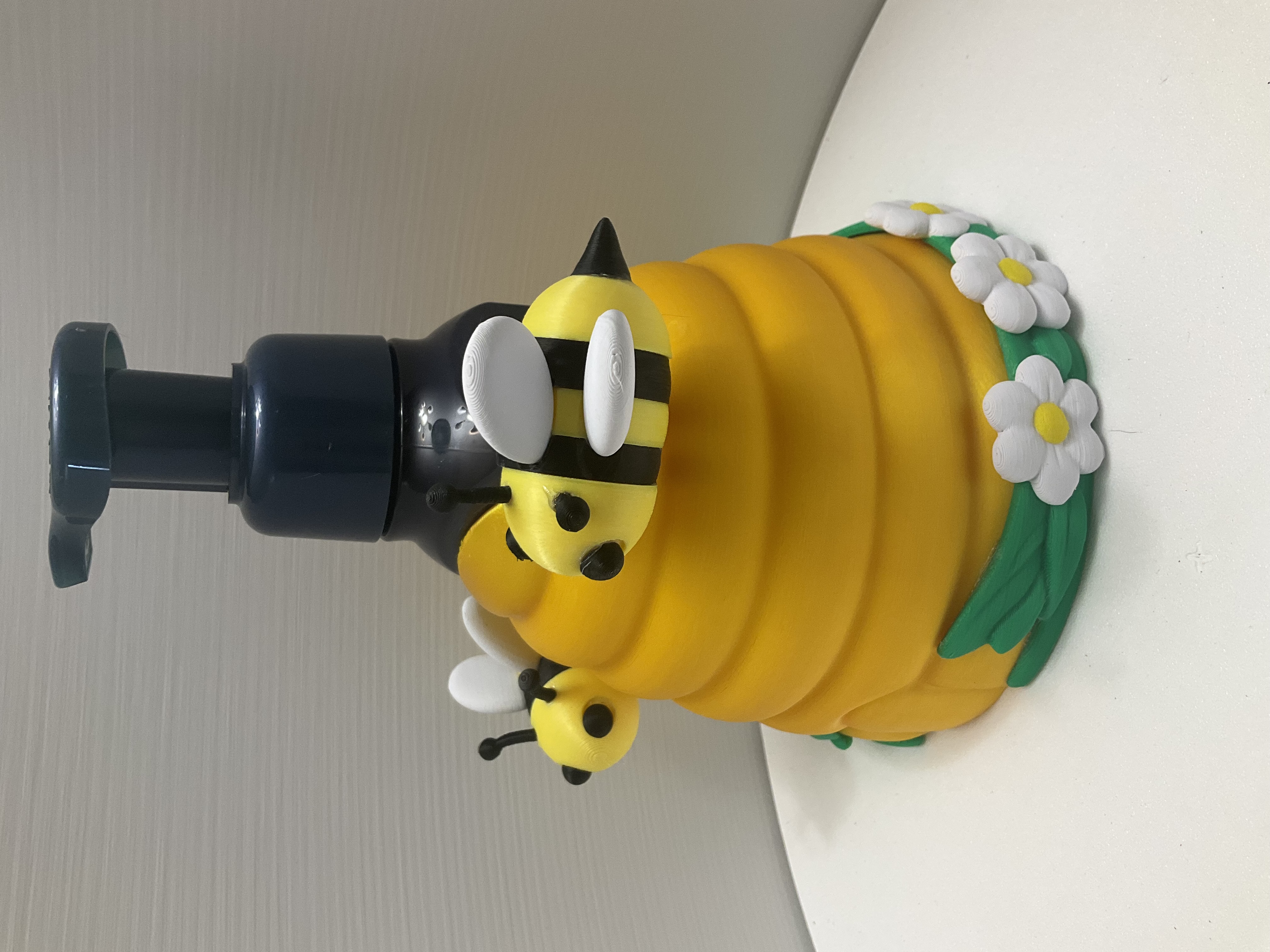 Side angle of beehive holder showing striped bee figure, white daisies, and green leaf base