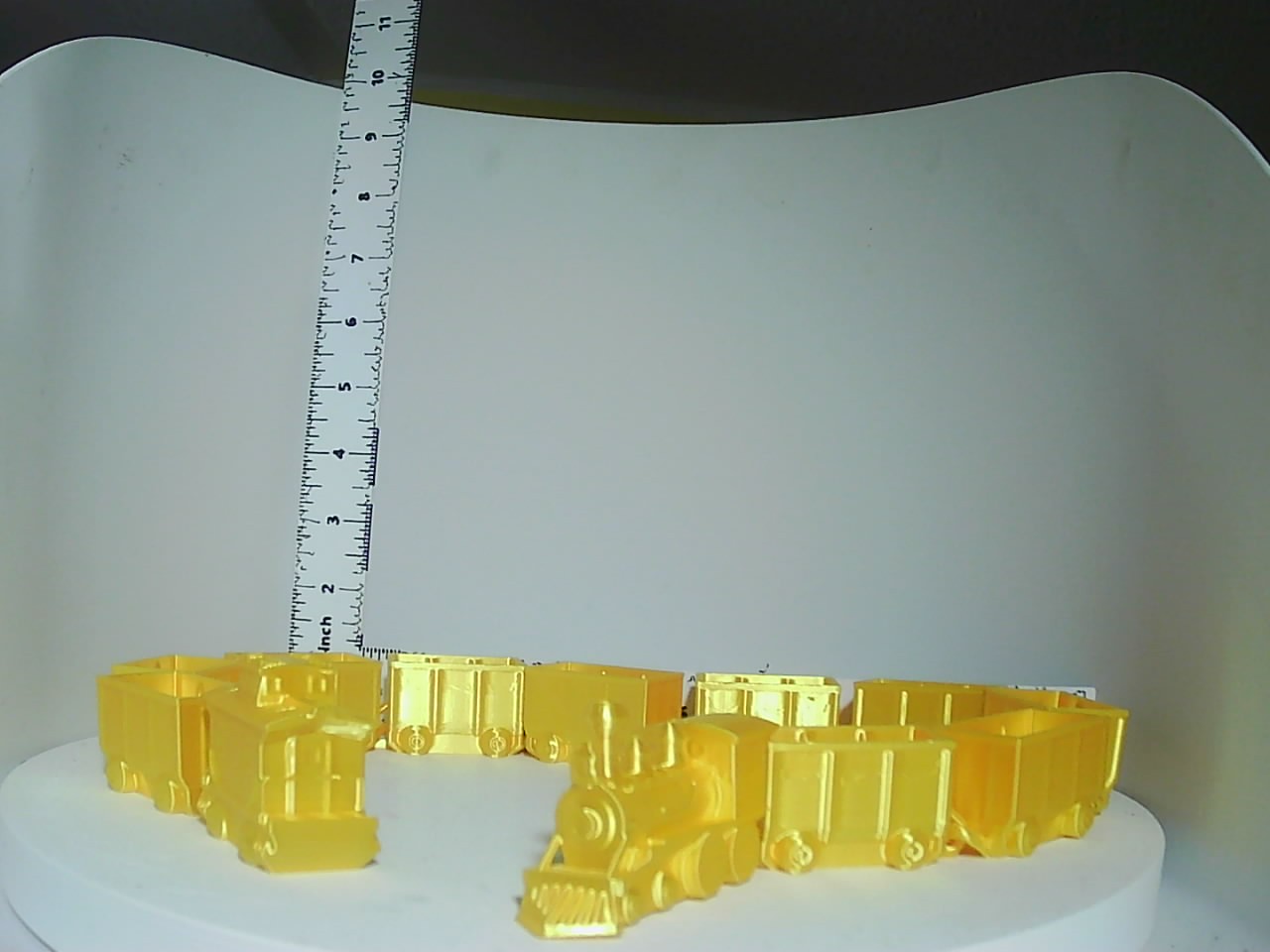 Bright yellow 3D-printed toy train set with locomotive and linked cargo cars on white surface