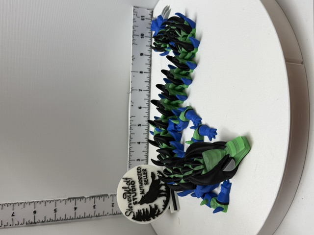 Full-length articulated dragon in black, blue, and green with ruler for scale