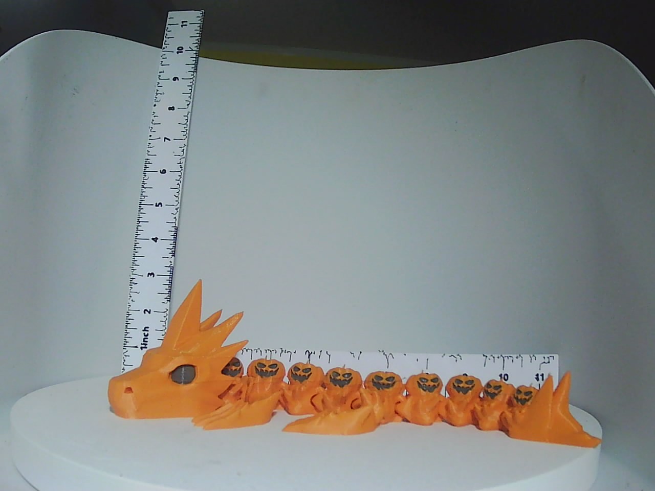 Orange articulated dragon with jack-o-lantern spine segments shown beside a ruler for scale