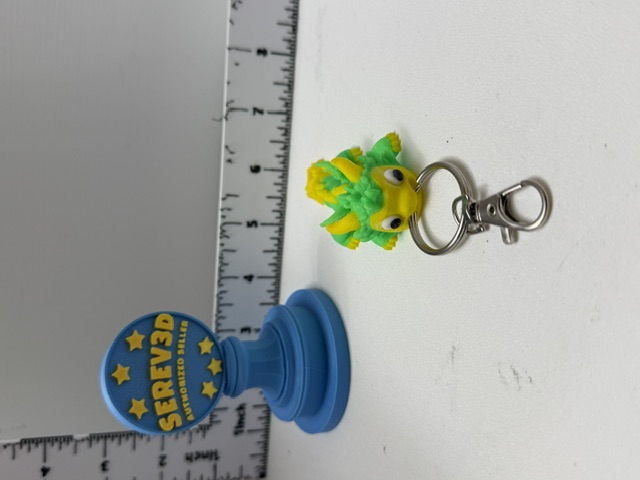 Green and yellow 3D printed dragon head keychain with silver swivel clip on white surface