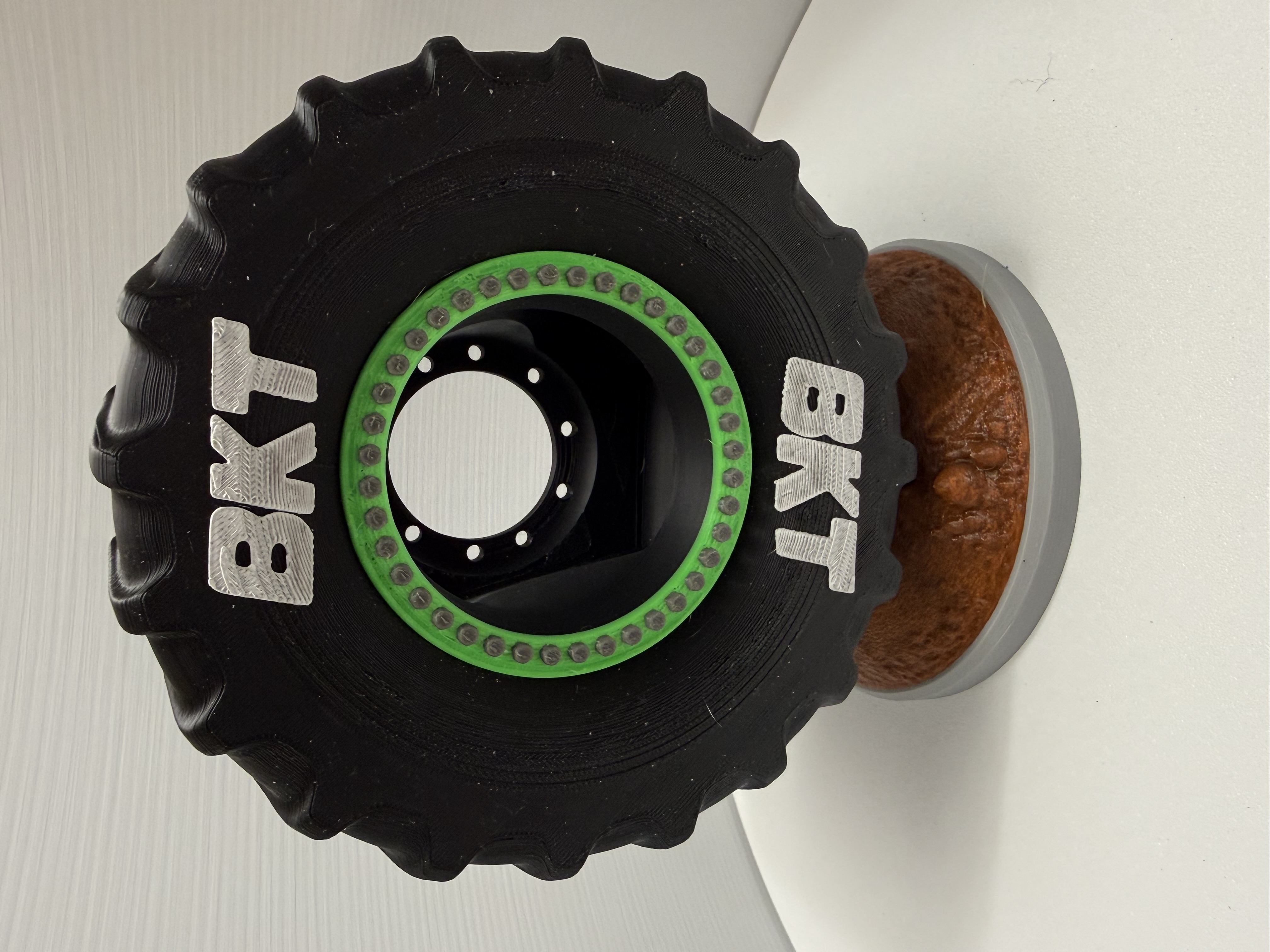 Black tractor tire desk sculpture with green ring displayed on textured brown soil base
