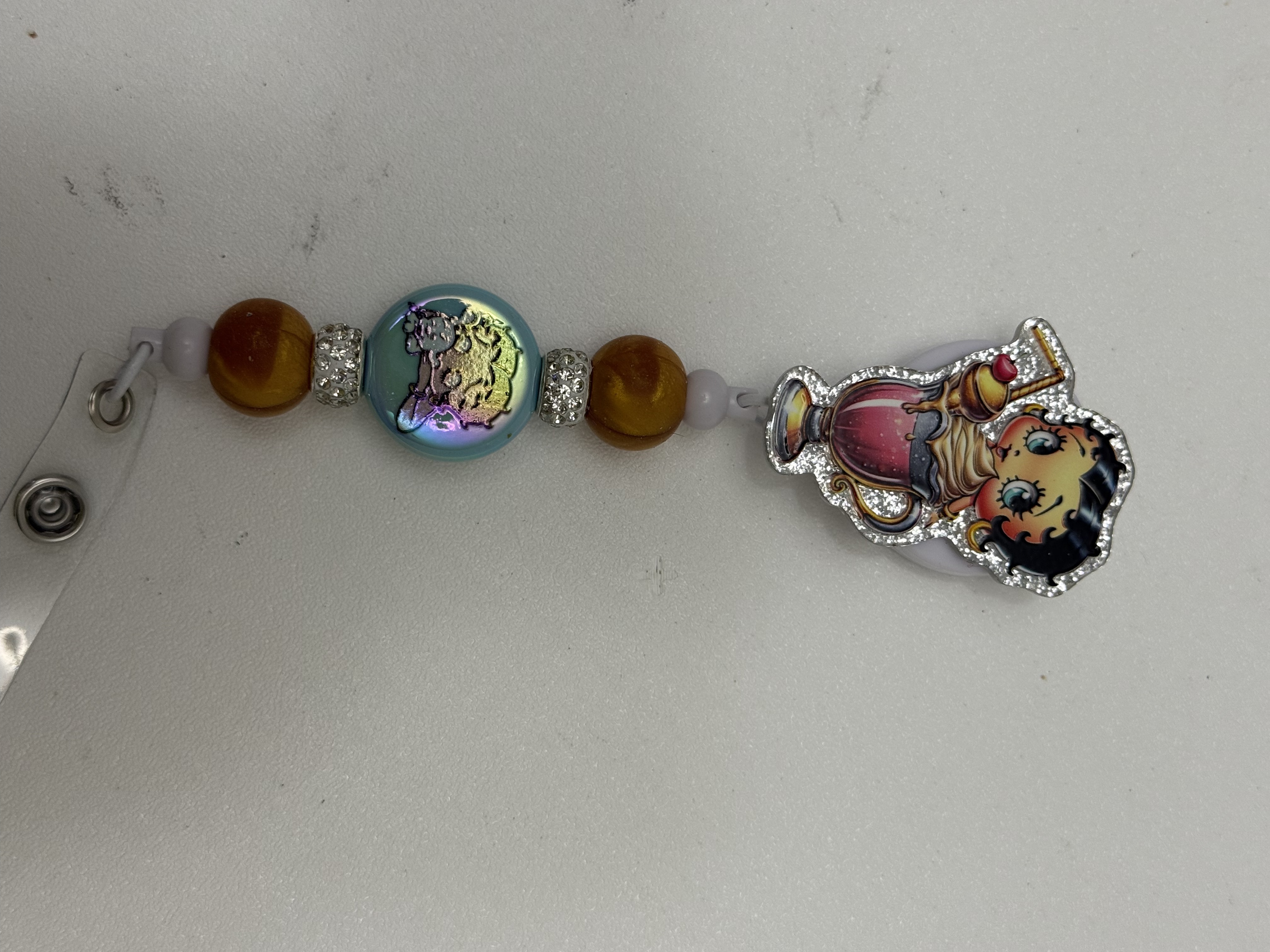Beaded badge reel with amber beads, iridescent coin bead, and glitter-edged retro pin-up acrylic charm
