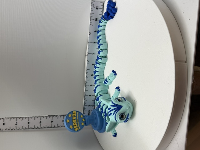 Mint and blue articulated lizard figurine with segmented flexing tail displayed next to a ruler