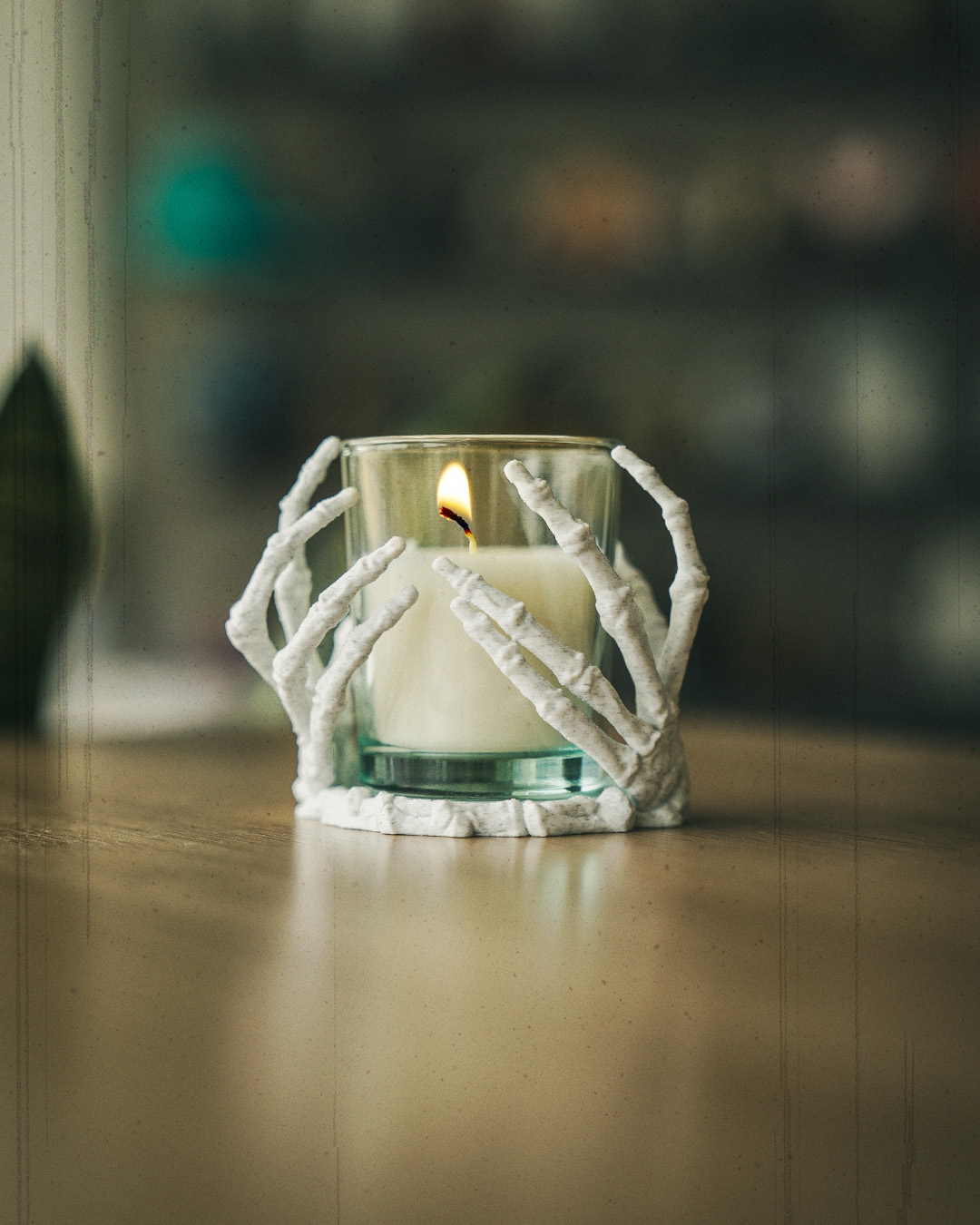 White skeletal hands candle holder cradling a lit glass votive on a wood surface