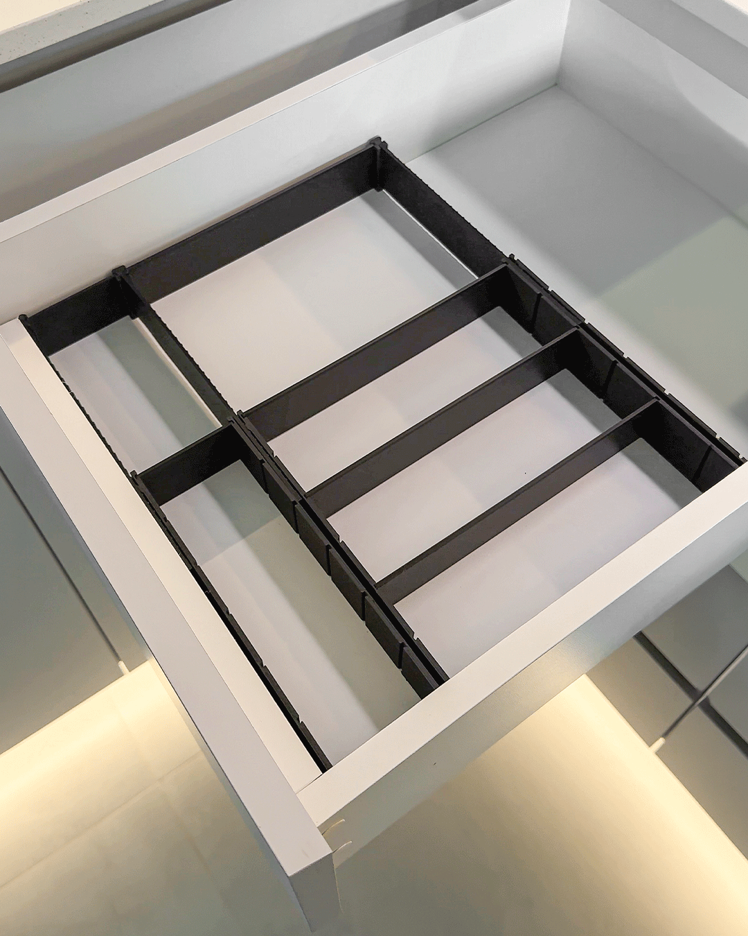 Dark 3D printed drawer dividers arranged in an empty white kitchen drawer from above